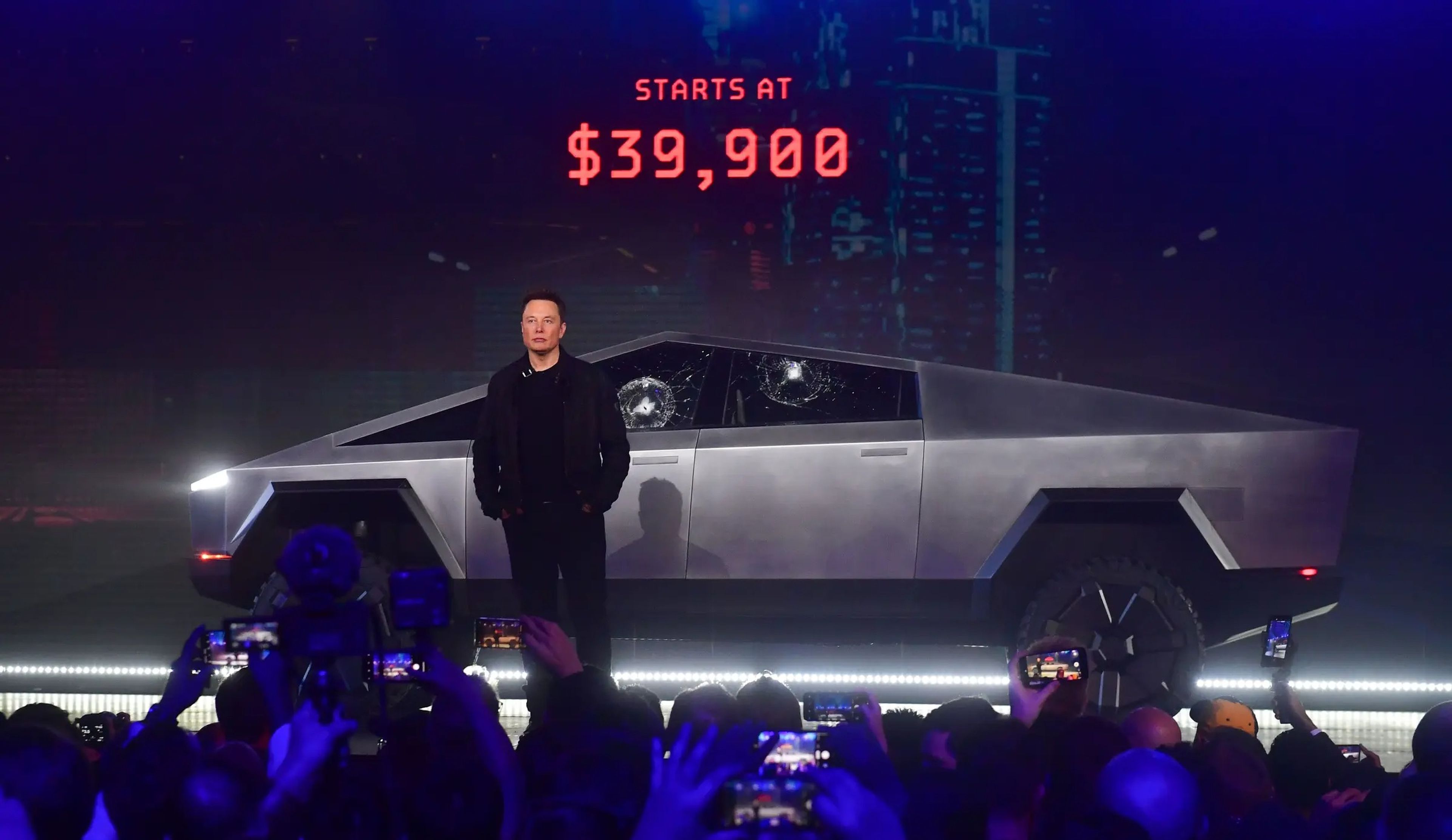 Elon Musk delante del Cybertruck totalmente eléctrico de Tesla en un escenario con el precio en luces rojas detrás de él.