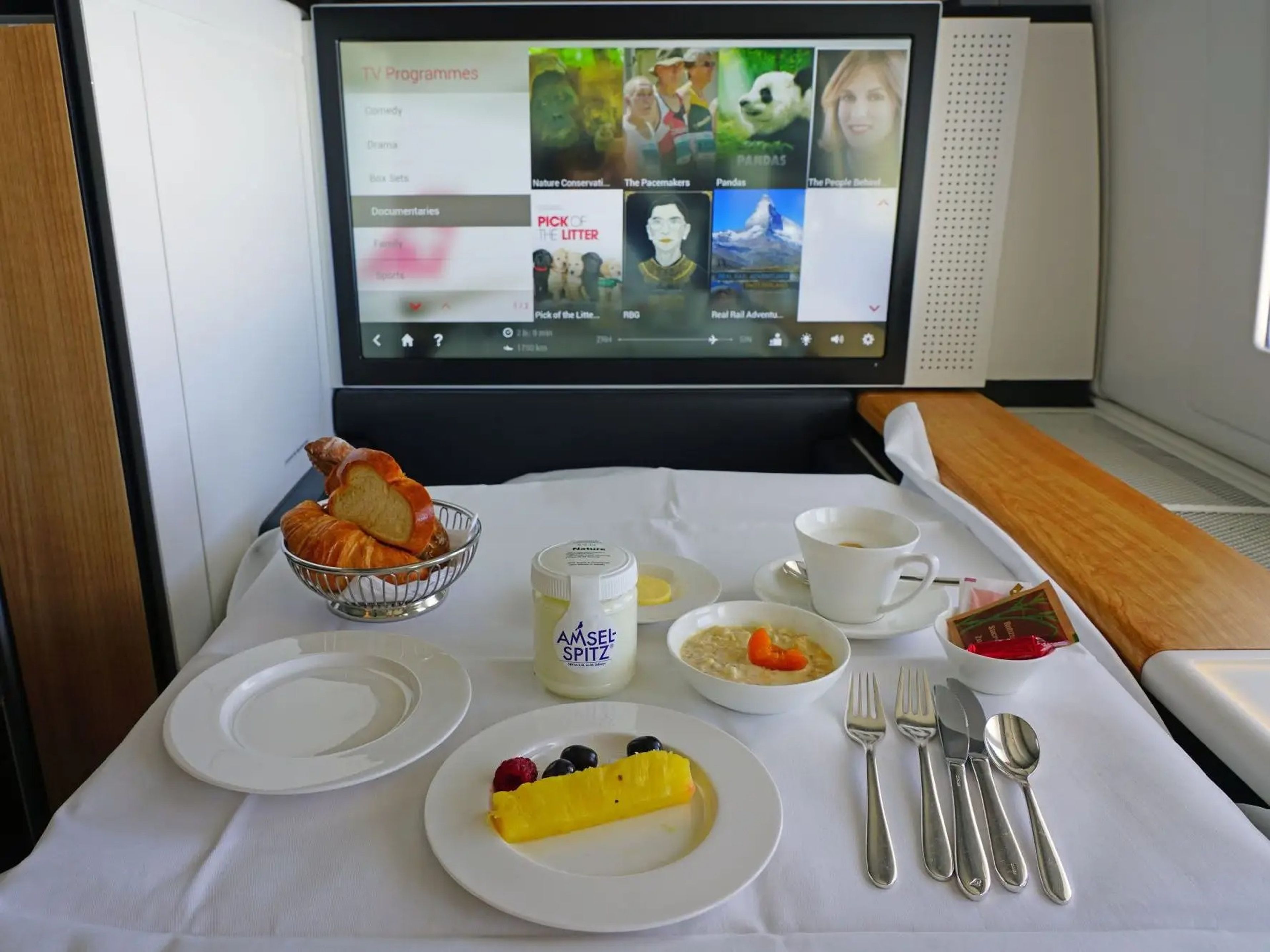 SWISS first class with with tray table full of food and television in view.
