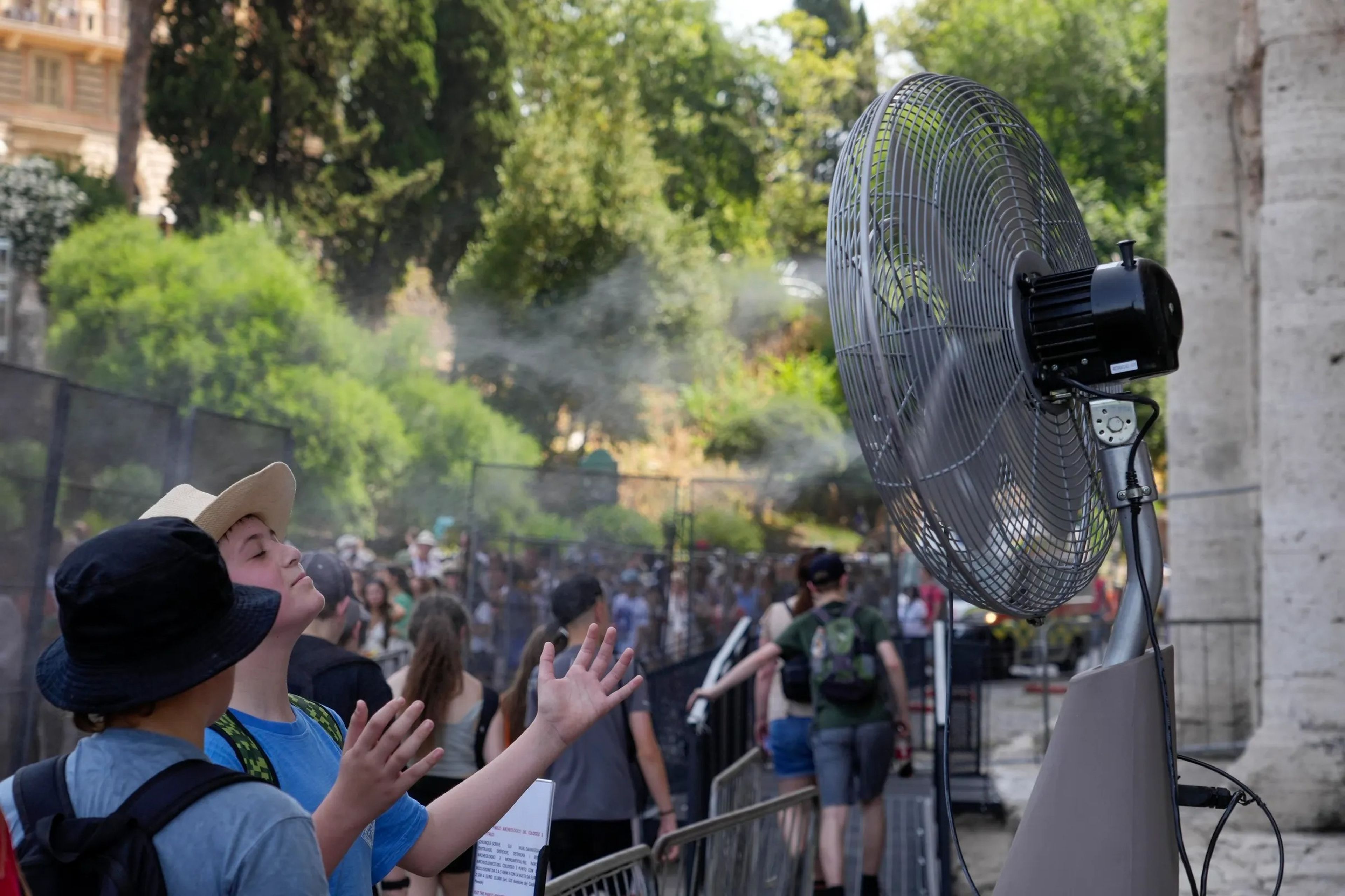 Tourists cool off near a fan as they queue to enter Rome's Colosseum. 