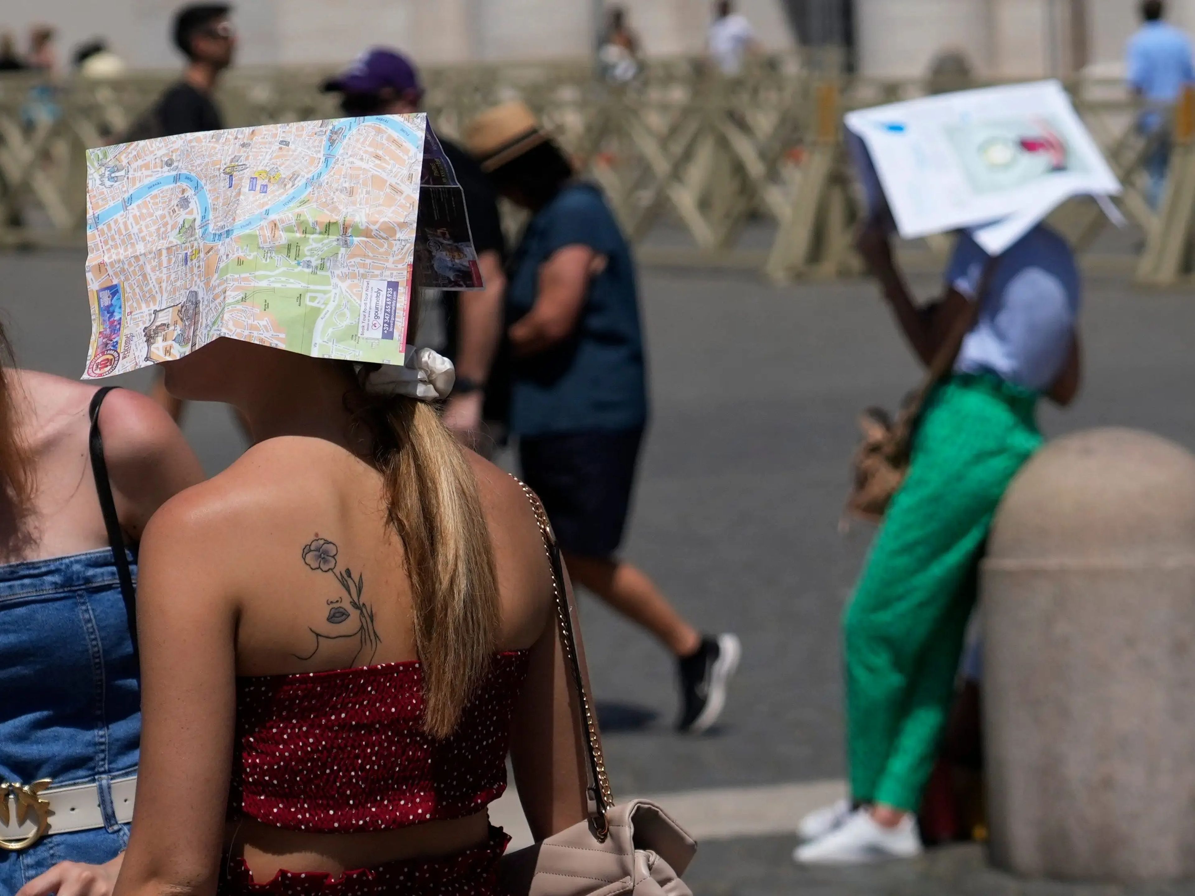 Turistas se cobijan bajo mapas mientras esperan el inicio de la oración del Ángelus del mediodía del Papa Francisco en la Plaza de San Pedro en la Ciudad del Vaticano, el 9 de julio de 2023.