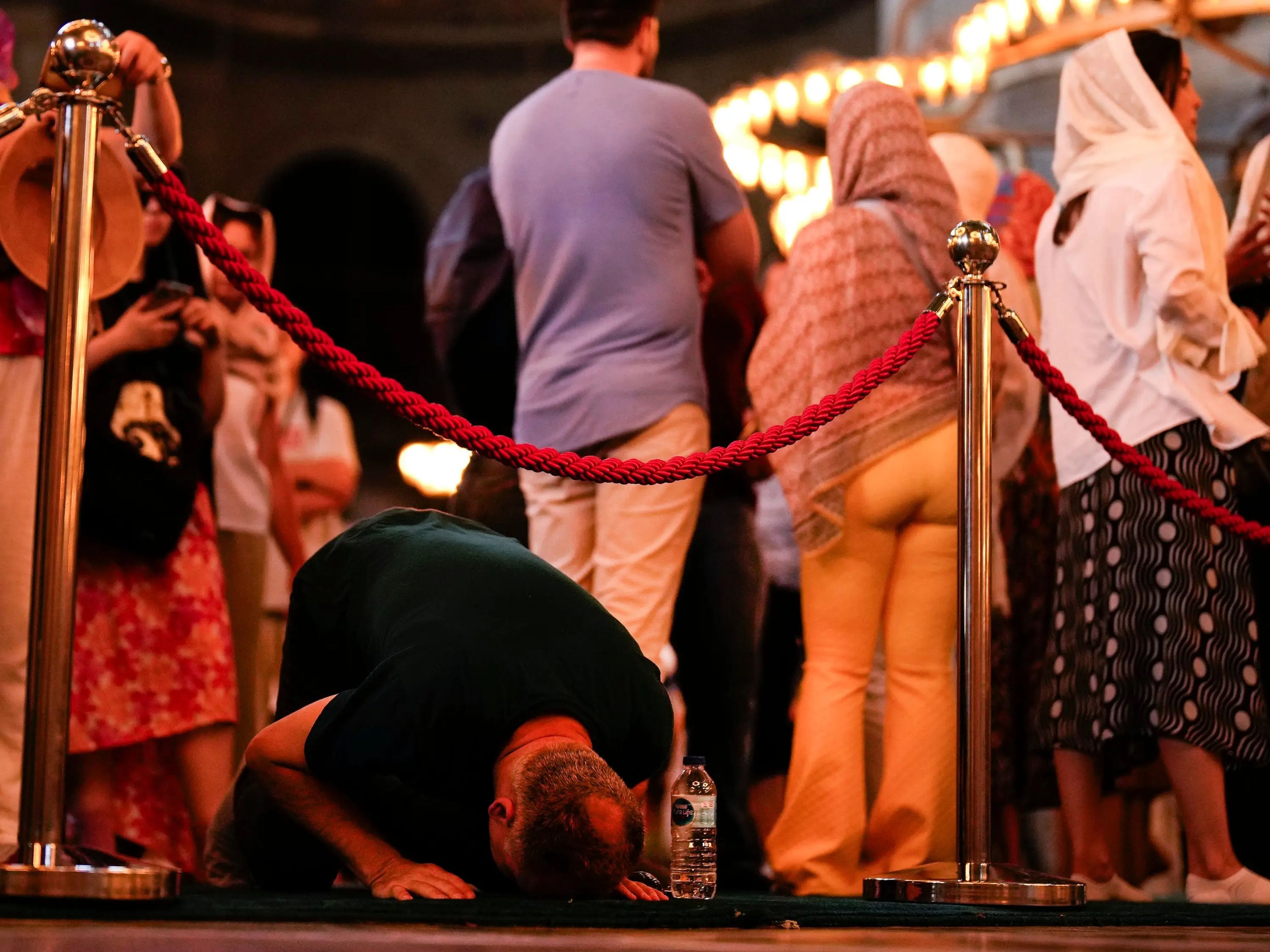 Un fiel reza mientras unos turistas visitan la mezquita de Santa Sofía, de la época bizantina, en Estambul, el 4 de julio de 2023.