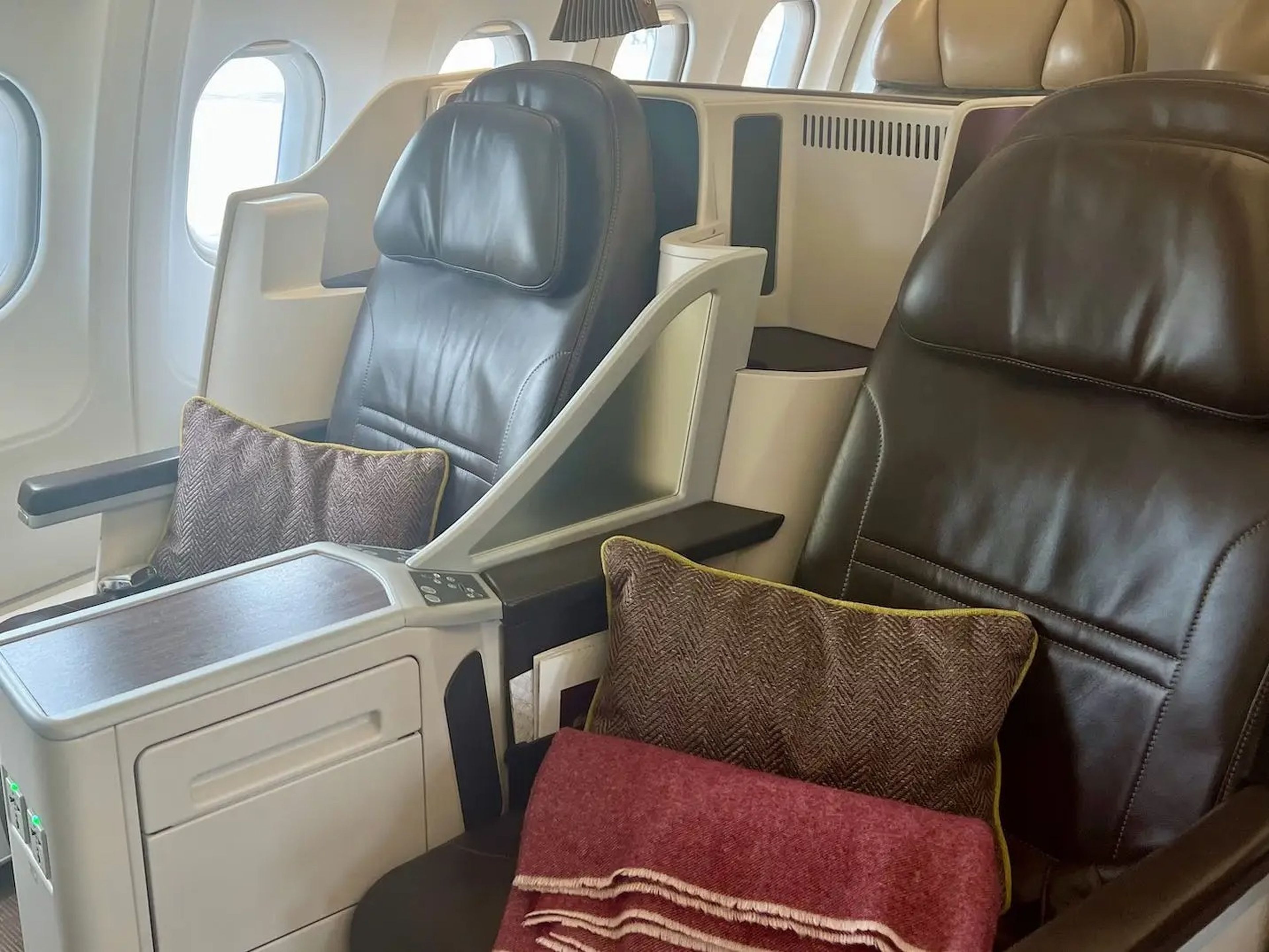 The brown lie-flat seats in 2x2 layout with pillows and blankets.