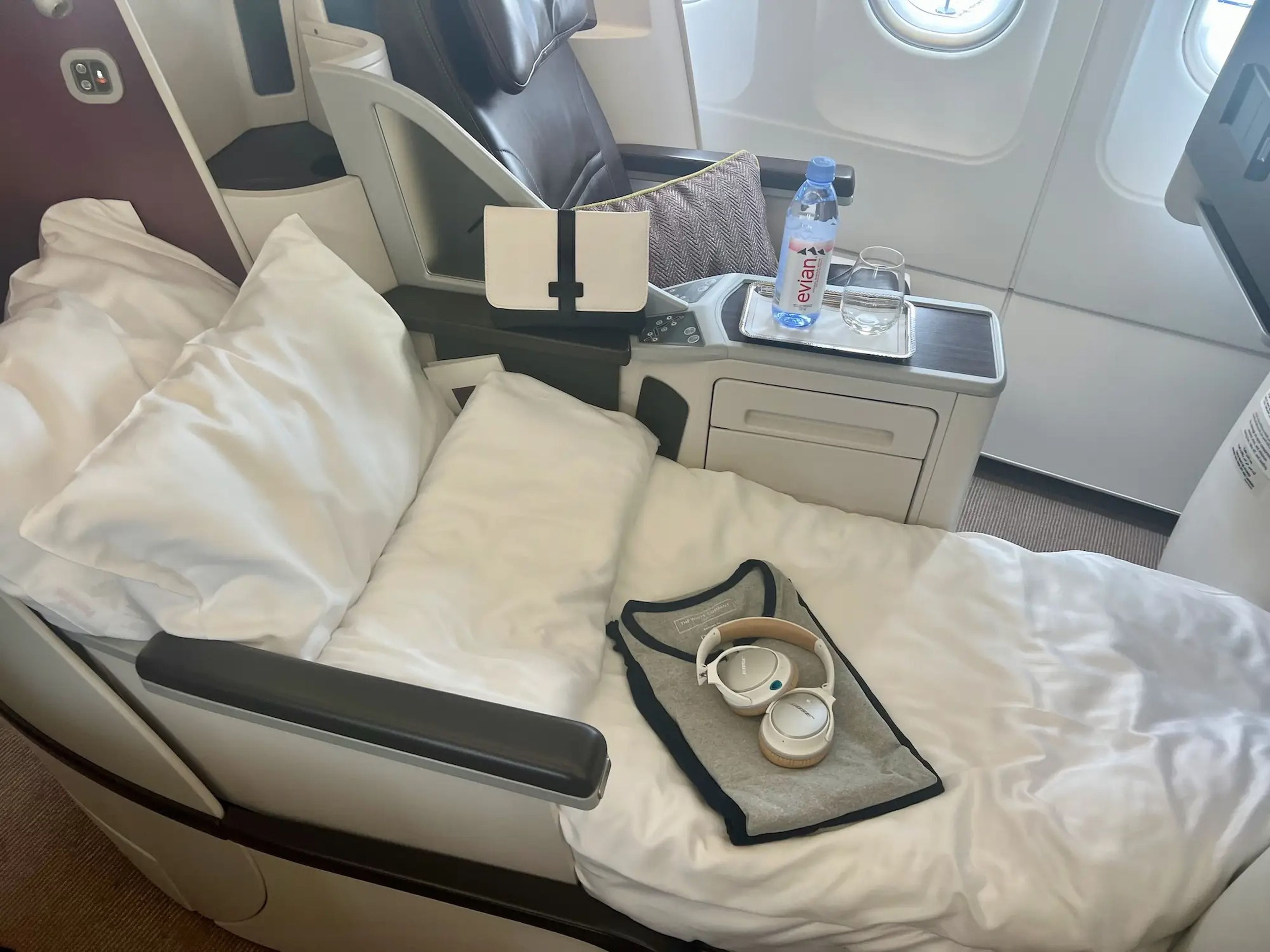 The business class seat in lie-flat mode with pajamas, a white amenity kit, and headphones