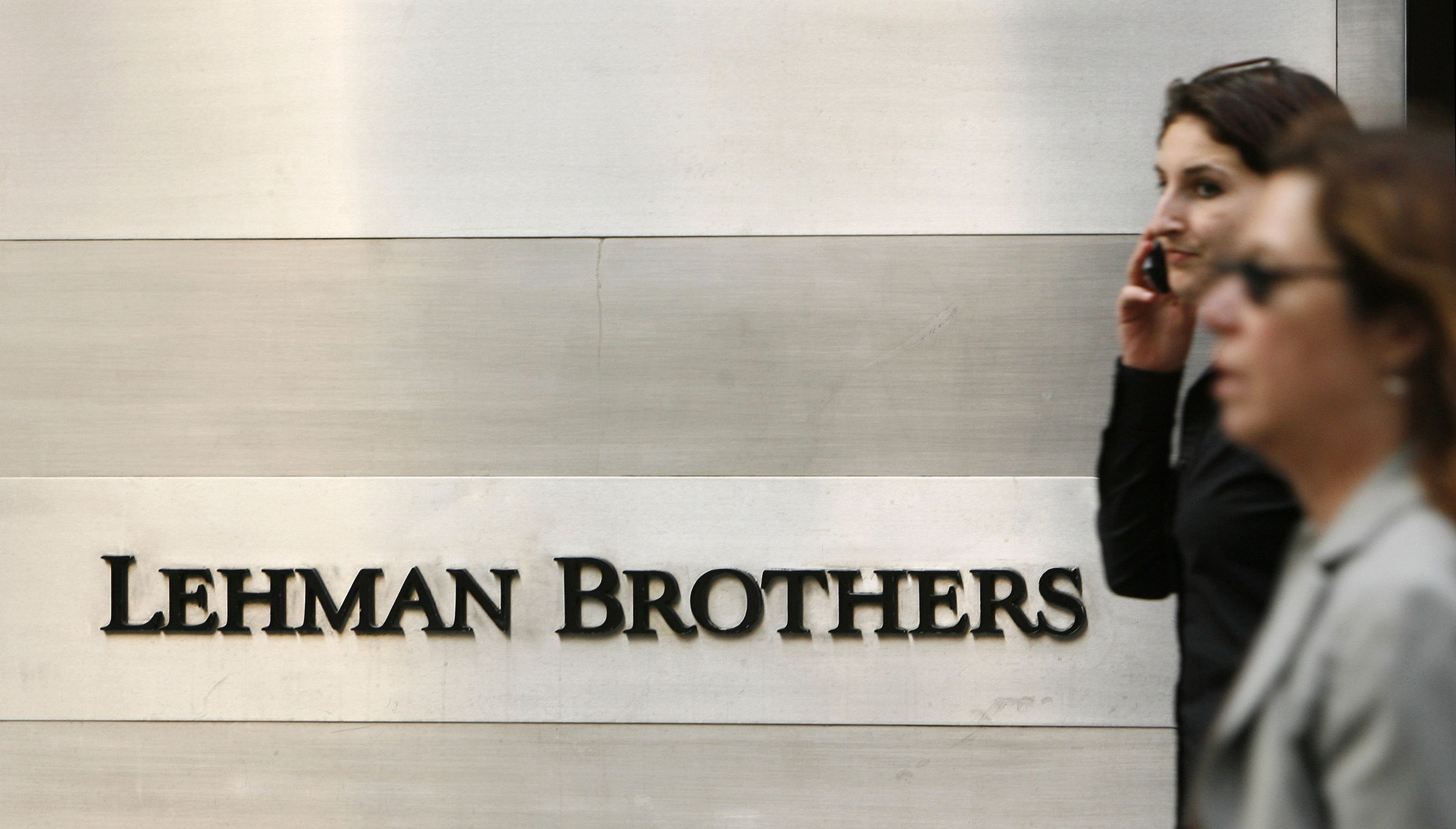 Dos mujeres andan por delante del cartel de Lehman Brothers, el banco que resultó en la mayor quiebra de Estados Unidos.