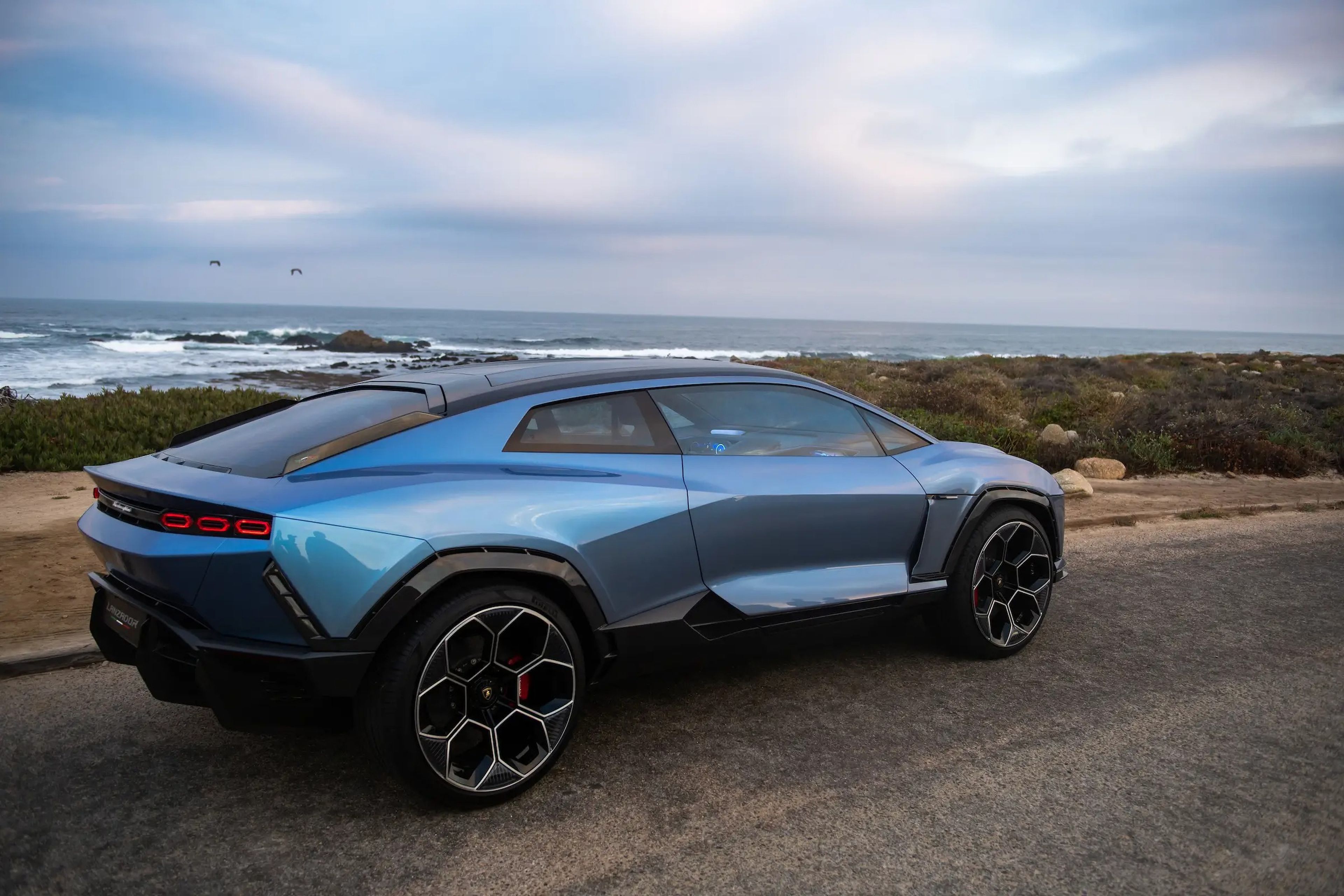 El prototipo Lamborghini Lanzador frente a una playa rocosa y un cielo azul nublado.