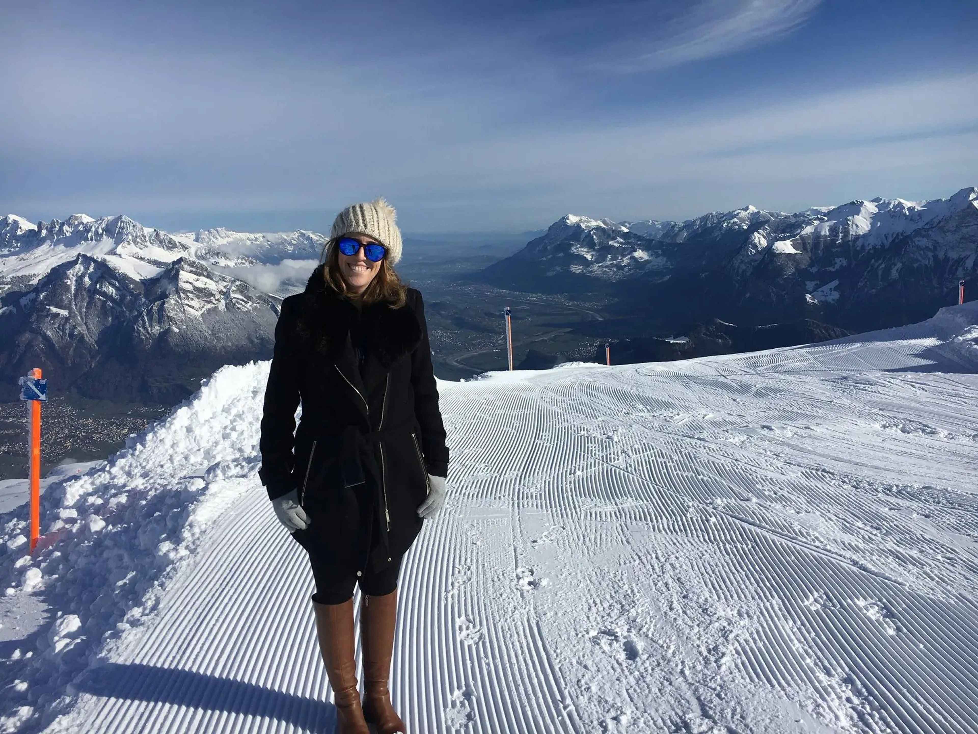 Michelle Gross standing outdoors in Switzerland with snow-covered mountains in the background. 