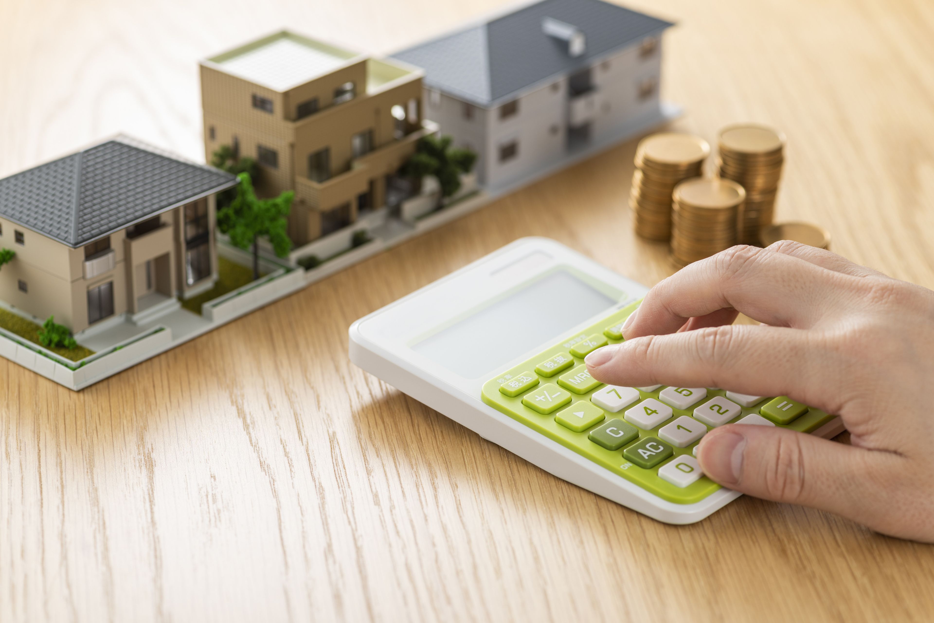 Una persona con una calculadora, varias monedas y una maqueta de varios edificios.
