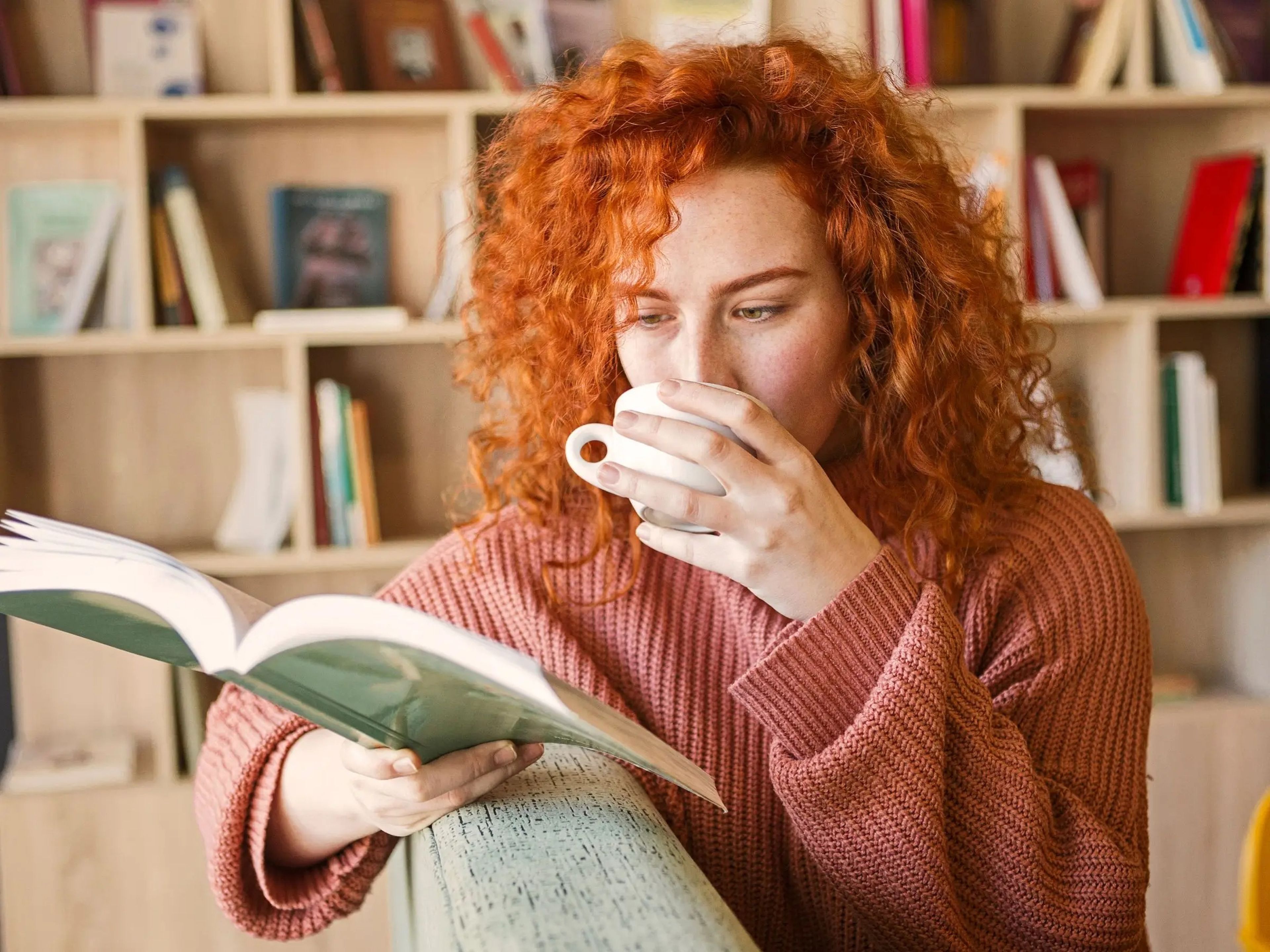 A woman reading a book and drinking coffee.