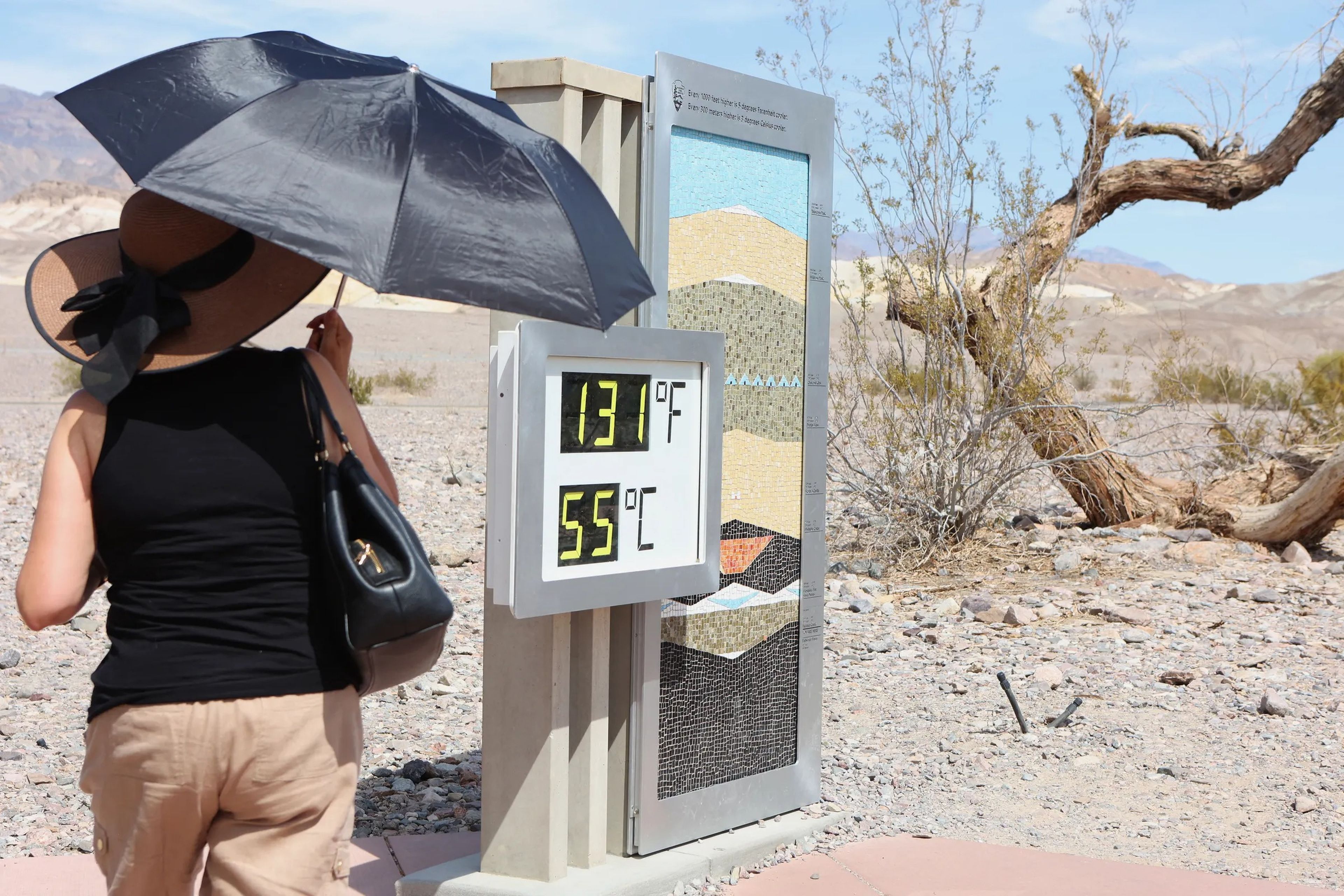 A woman stands near a digital display of an unofficial heat reading at Furnace Creek Visitor Center during a heat wave in Death Valley National Park, California, on July 16, 2023.
