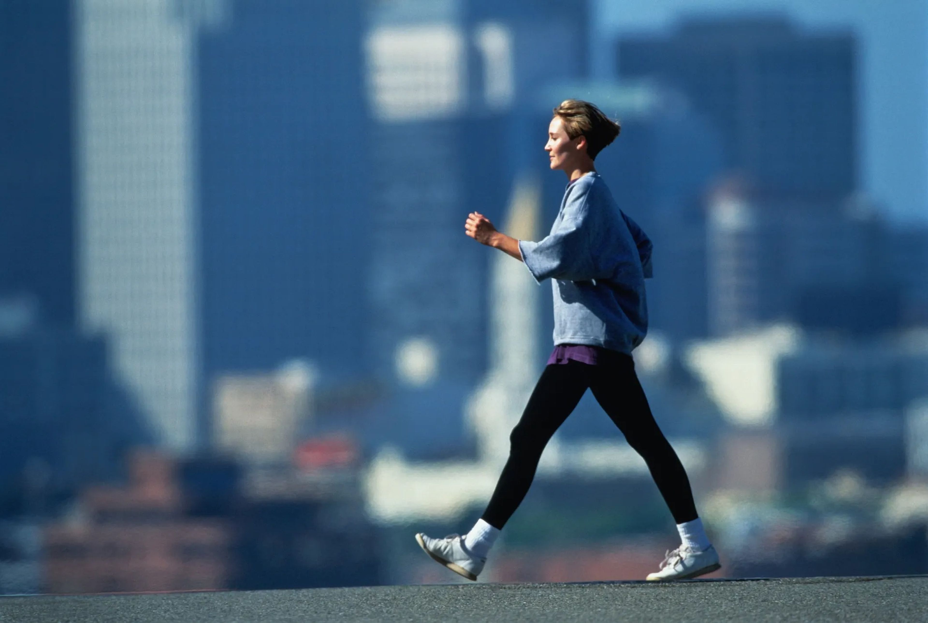 a woman walking at a brisk pace outside with a blurred skyline in the background