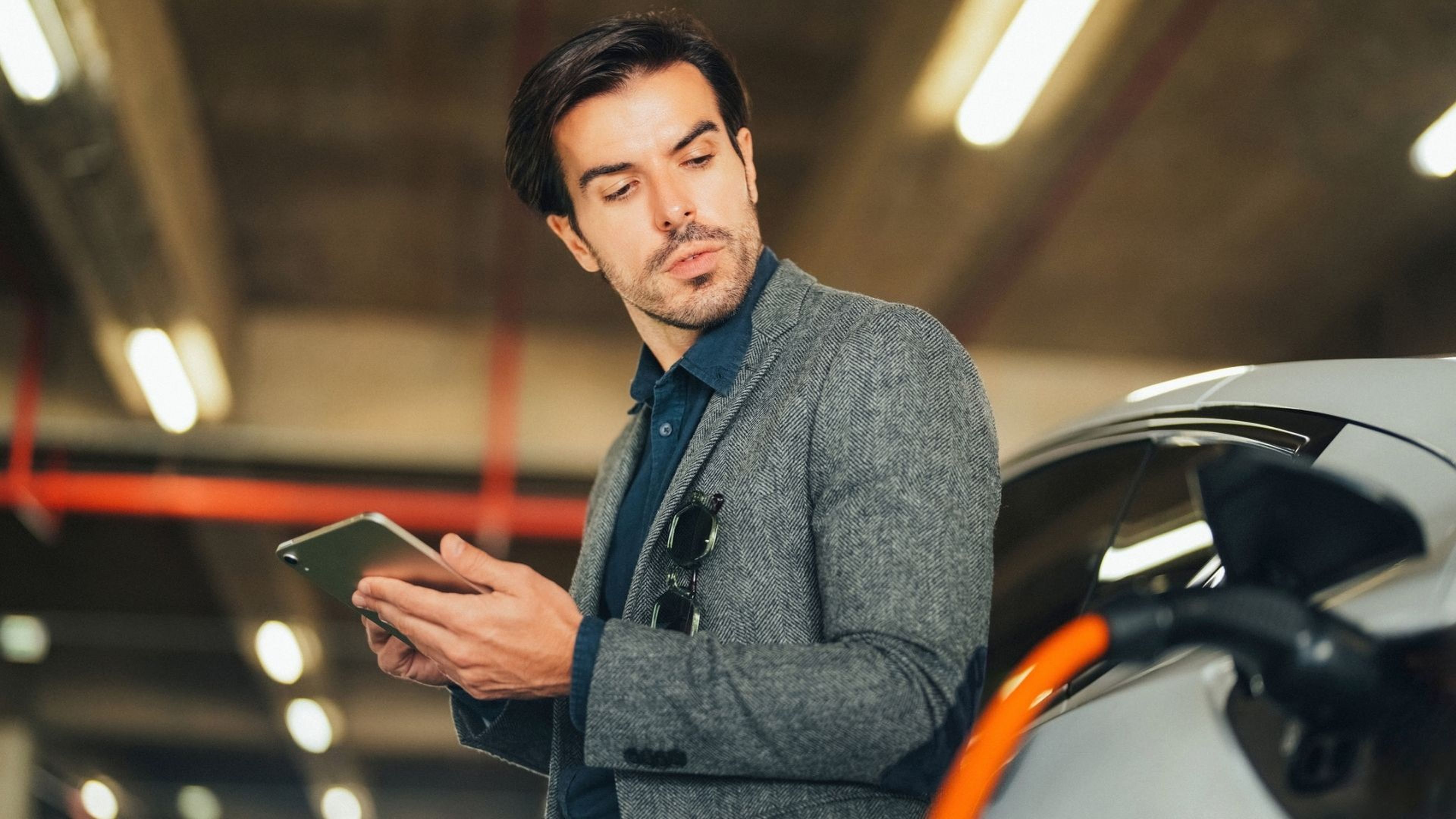 Un hombre consulta su tablet mientras se carga su coche eléctrico.