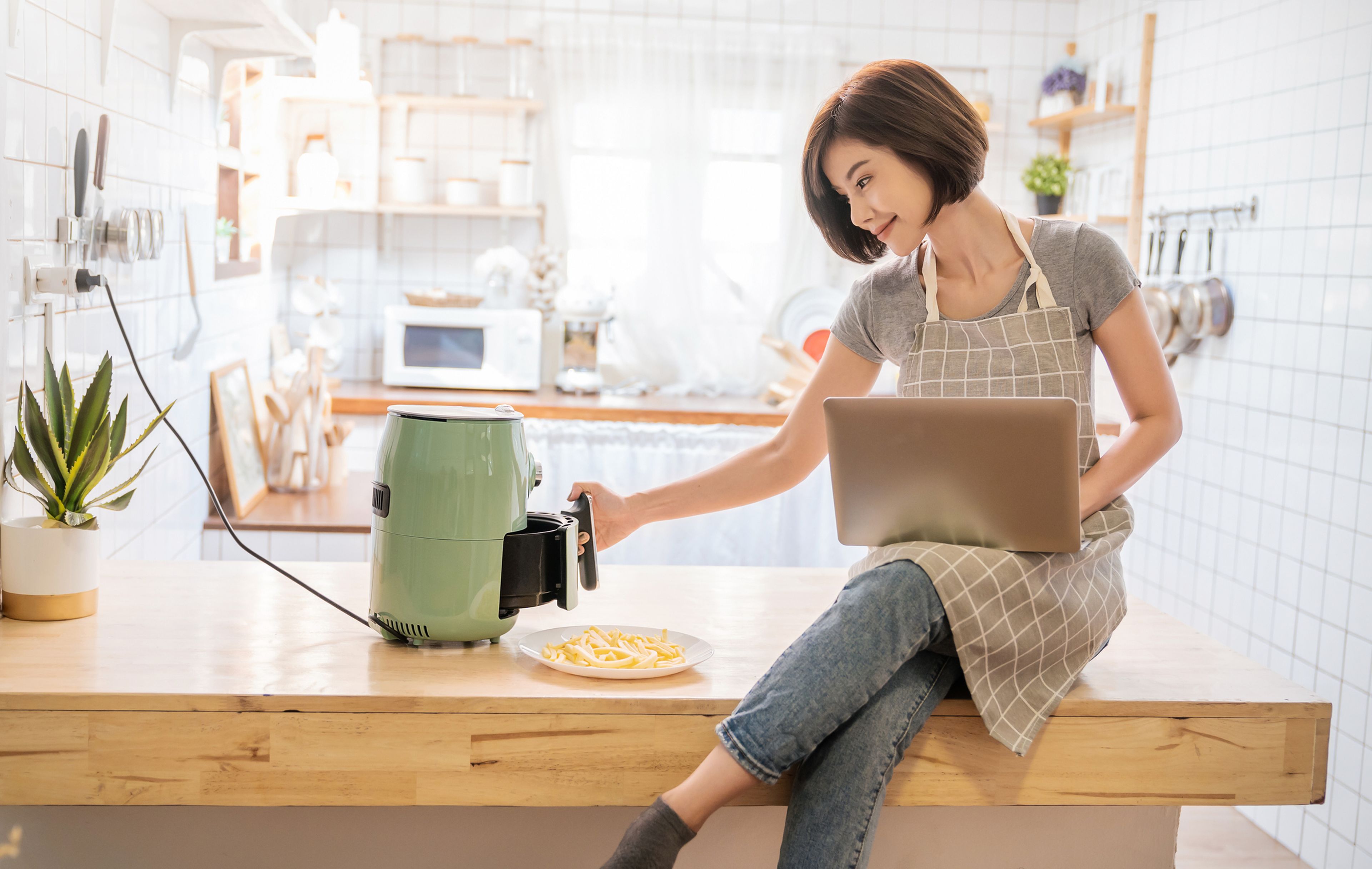 Una mujer con el ordenador, mientras cocina patatas en un robot.