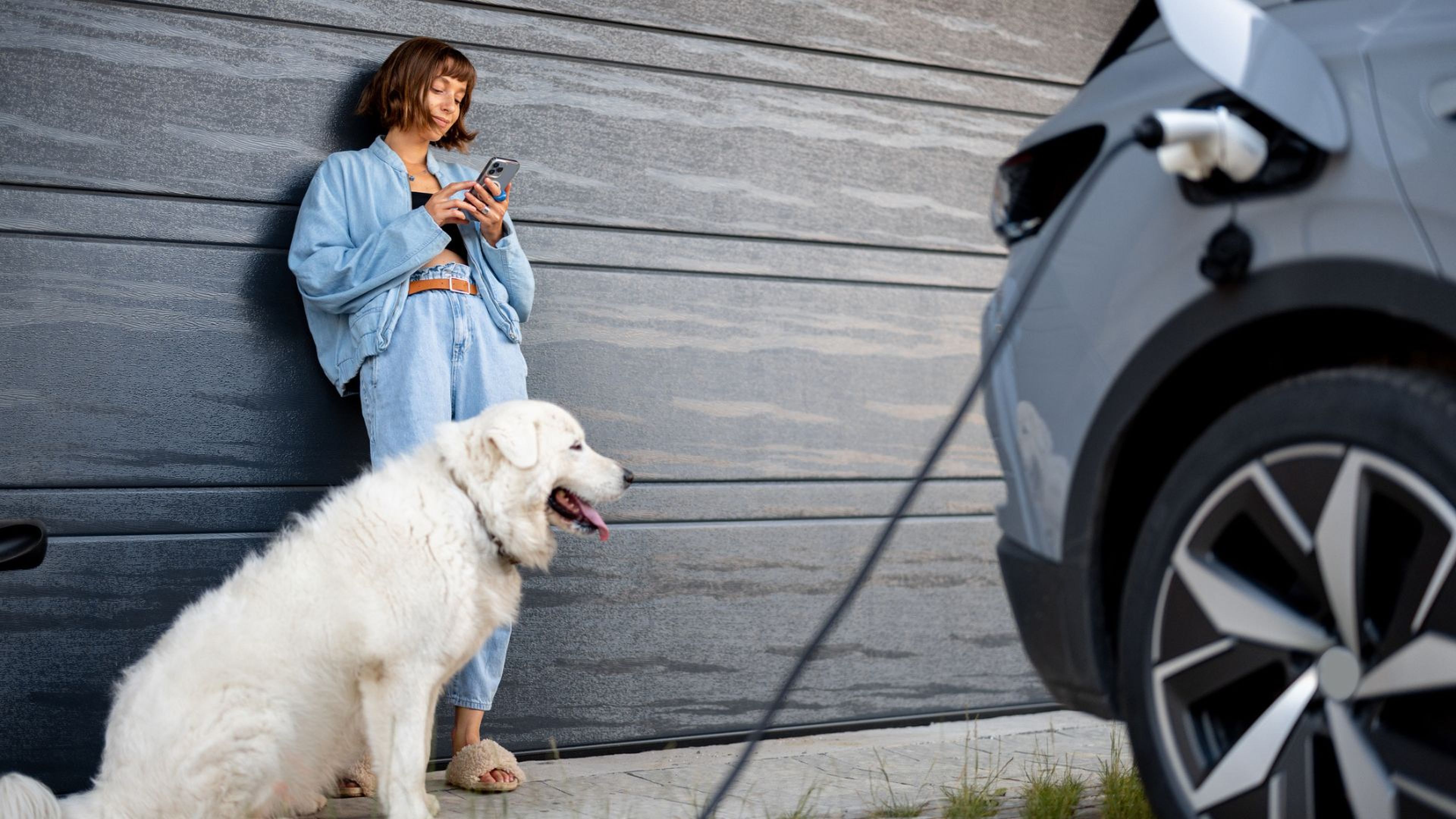 Una mujer y su perro esperan mientras se cara el coche eléctrico.