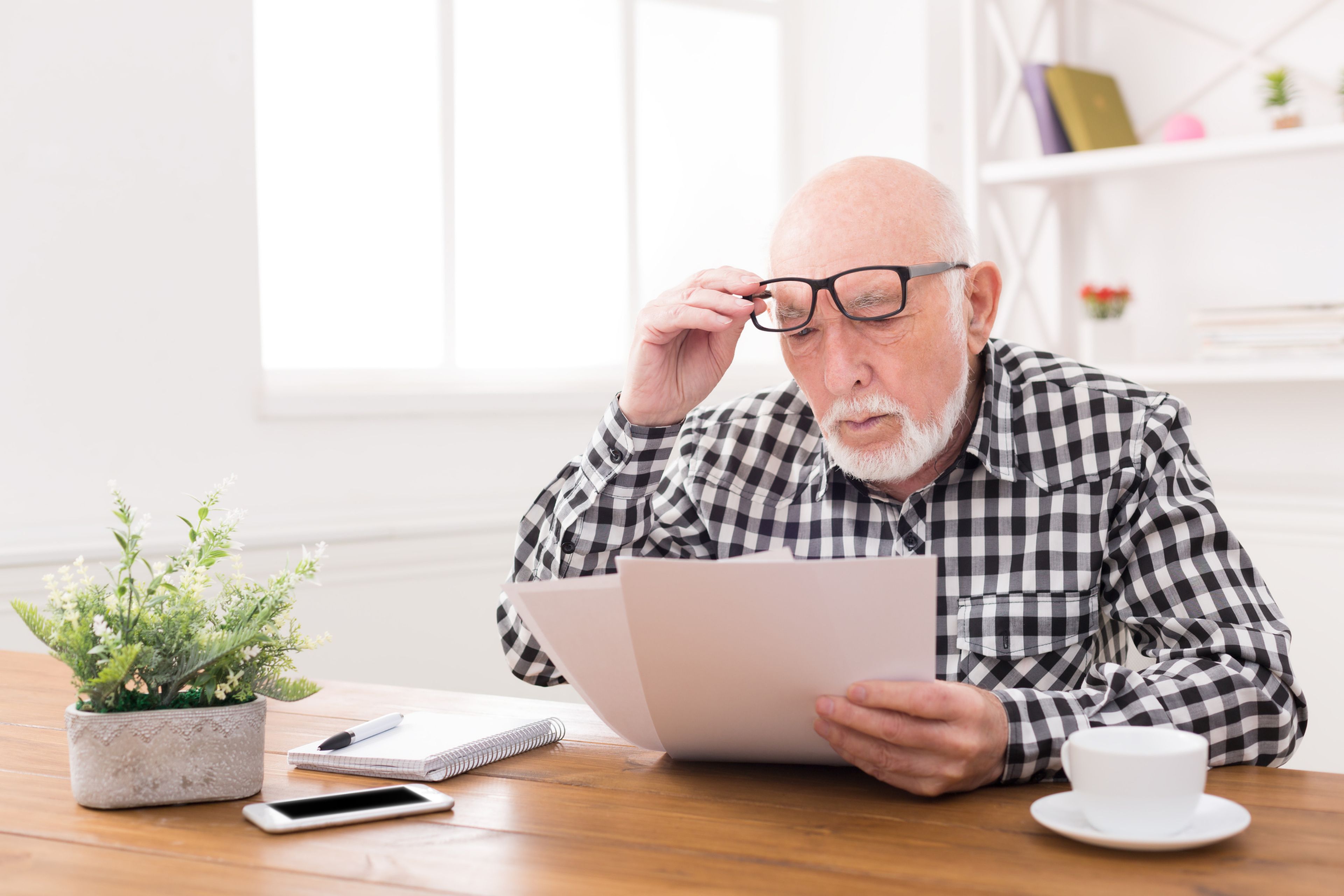 Pensionista, hombre mayor mira documentos con gafas