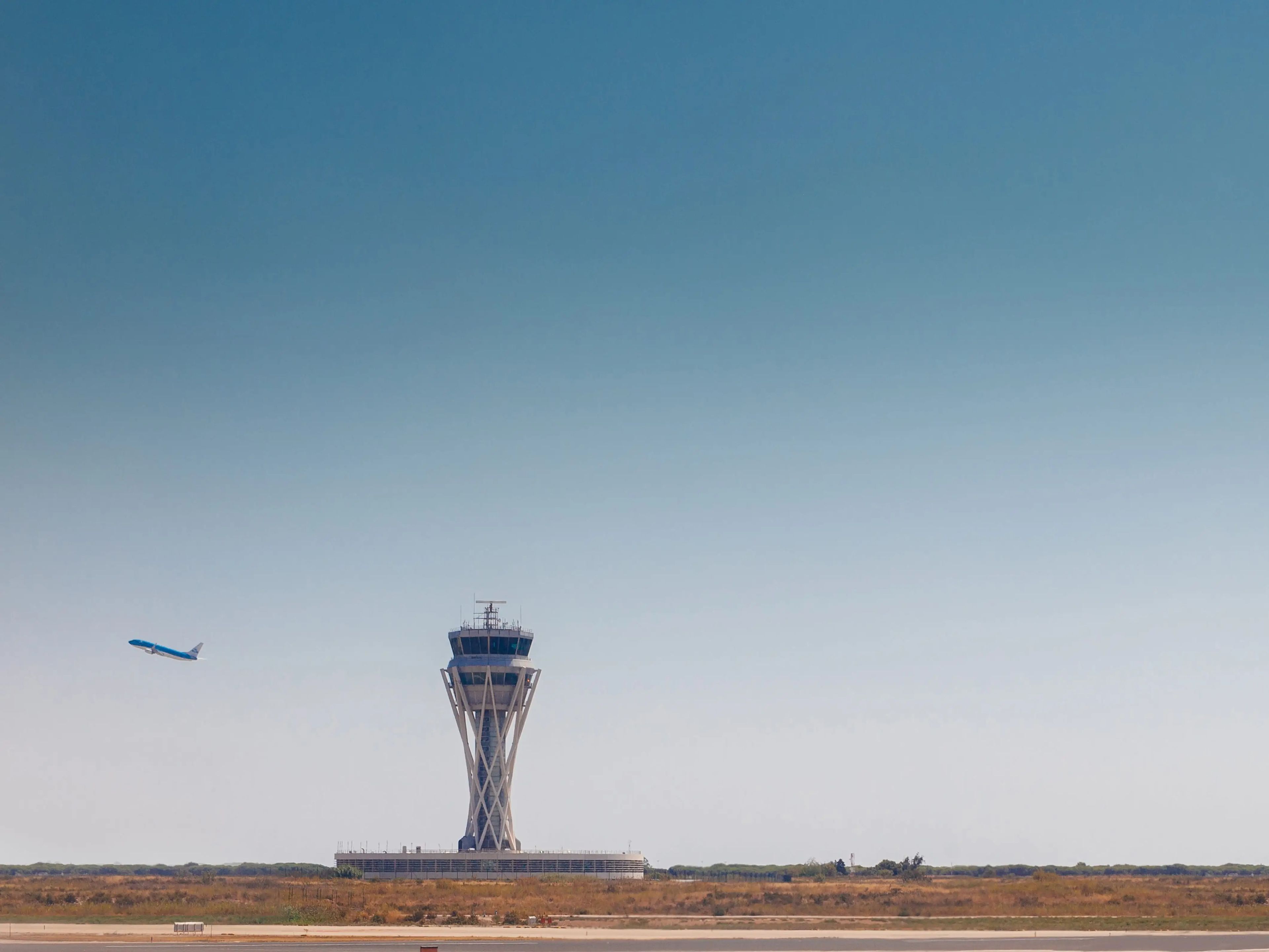 A plane takes off with an air traffic control tower in the foreground.