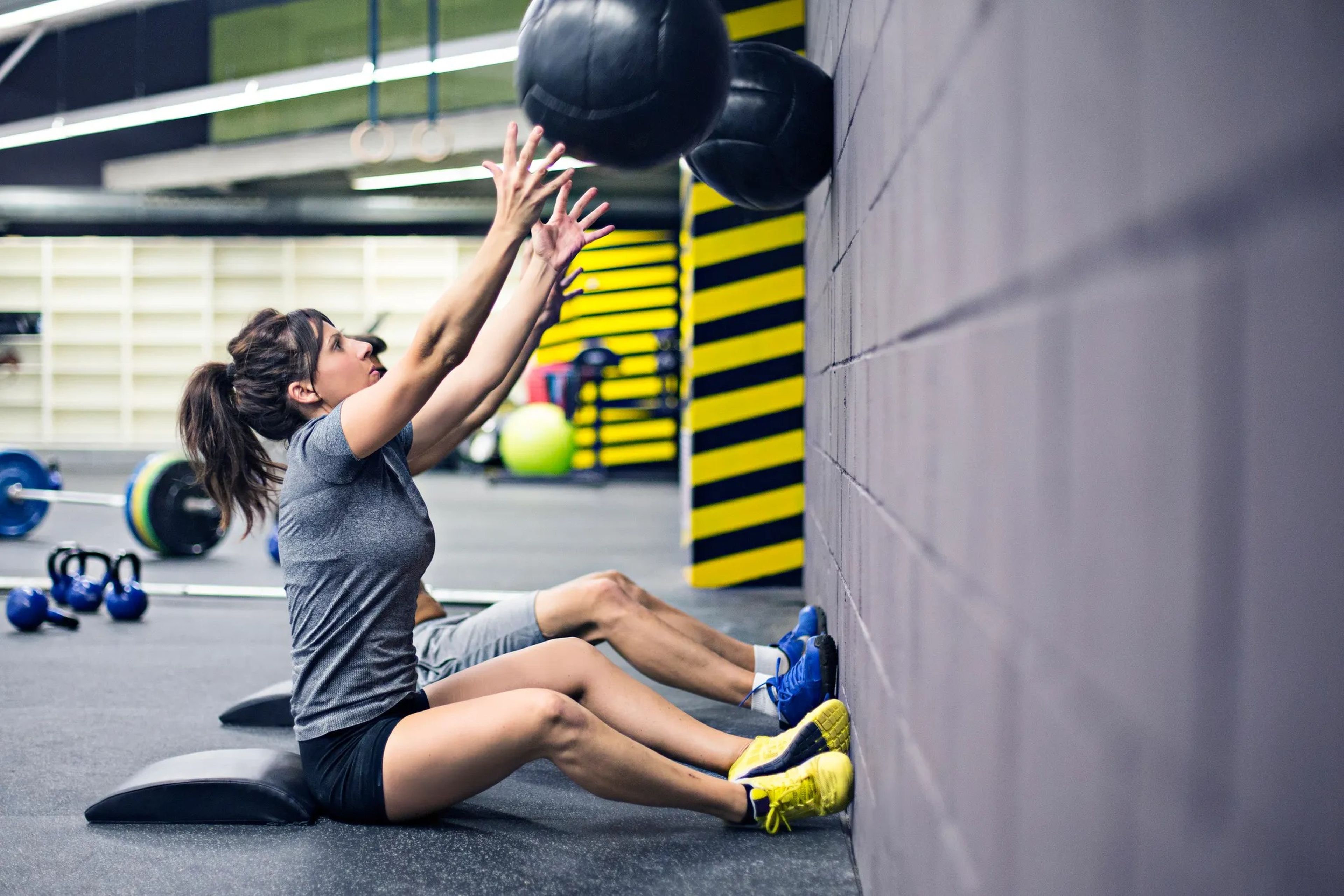 a woman and a man throwing a weighted medicine ball against a wall