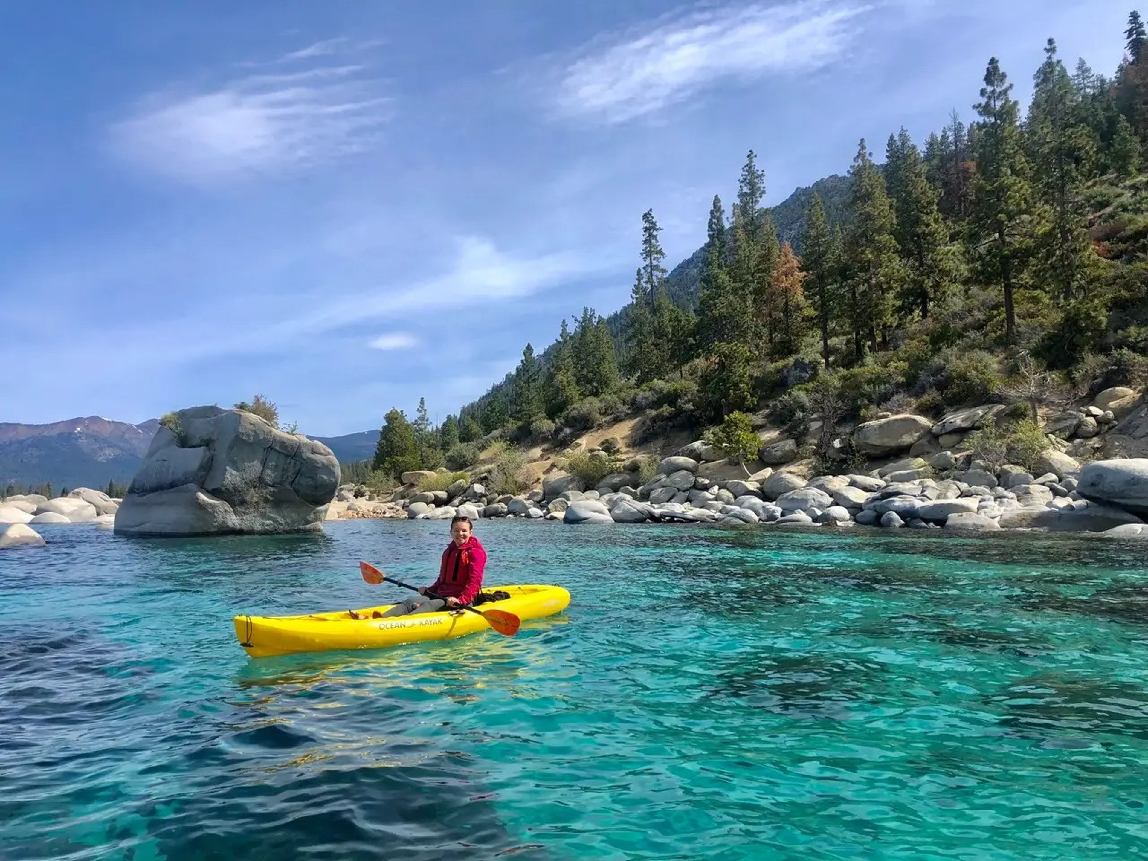 Author Nicole Jordan in a yellow boat on bright-blue waters in front of trees and rocks