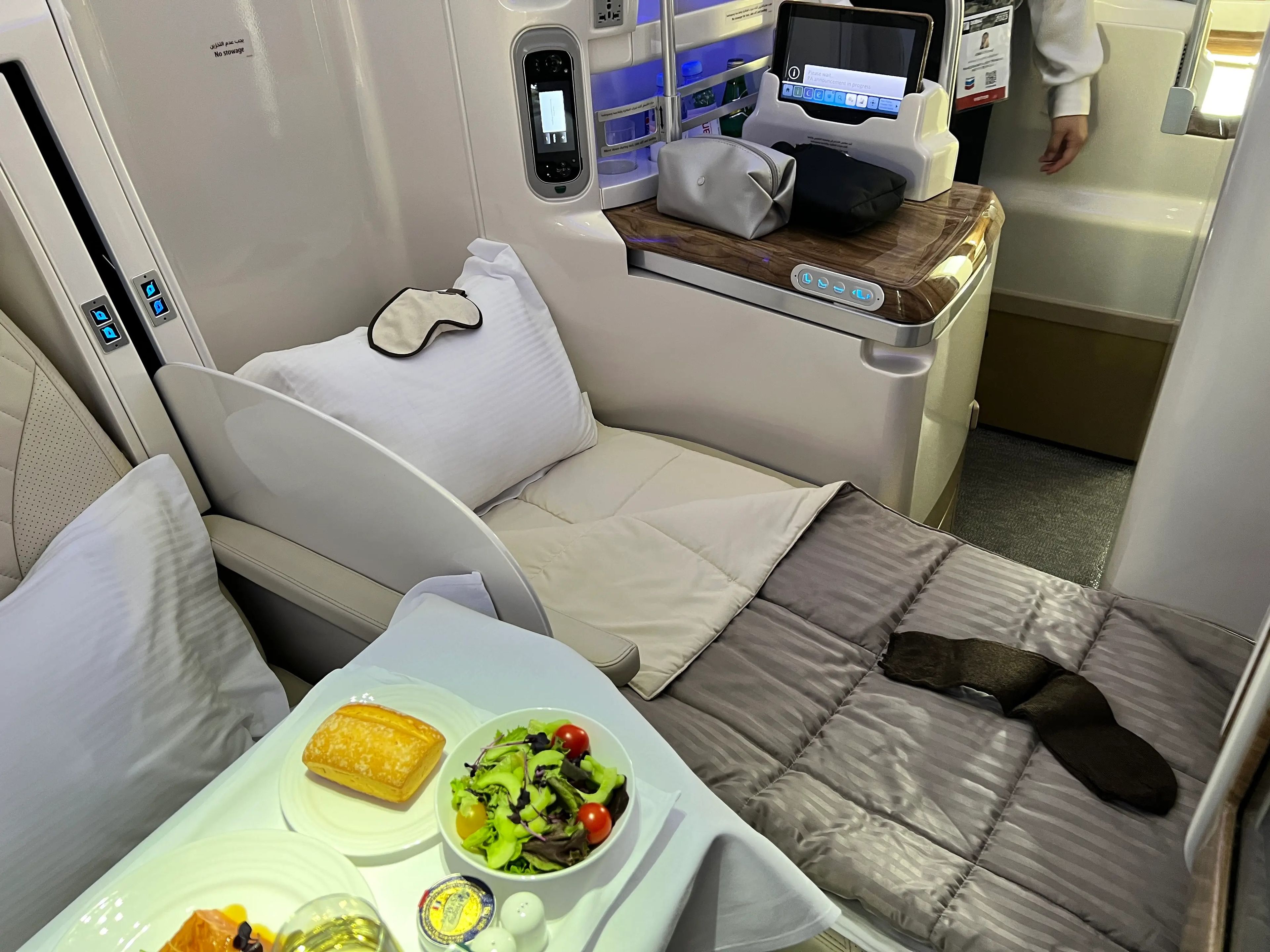 A business class seat in the middle of a Emirates A380 is set up as a lie-down bed with a comforter.