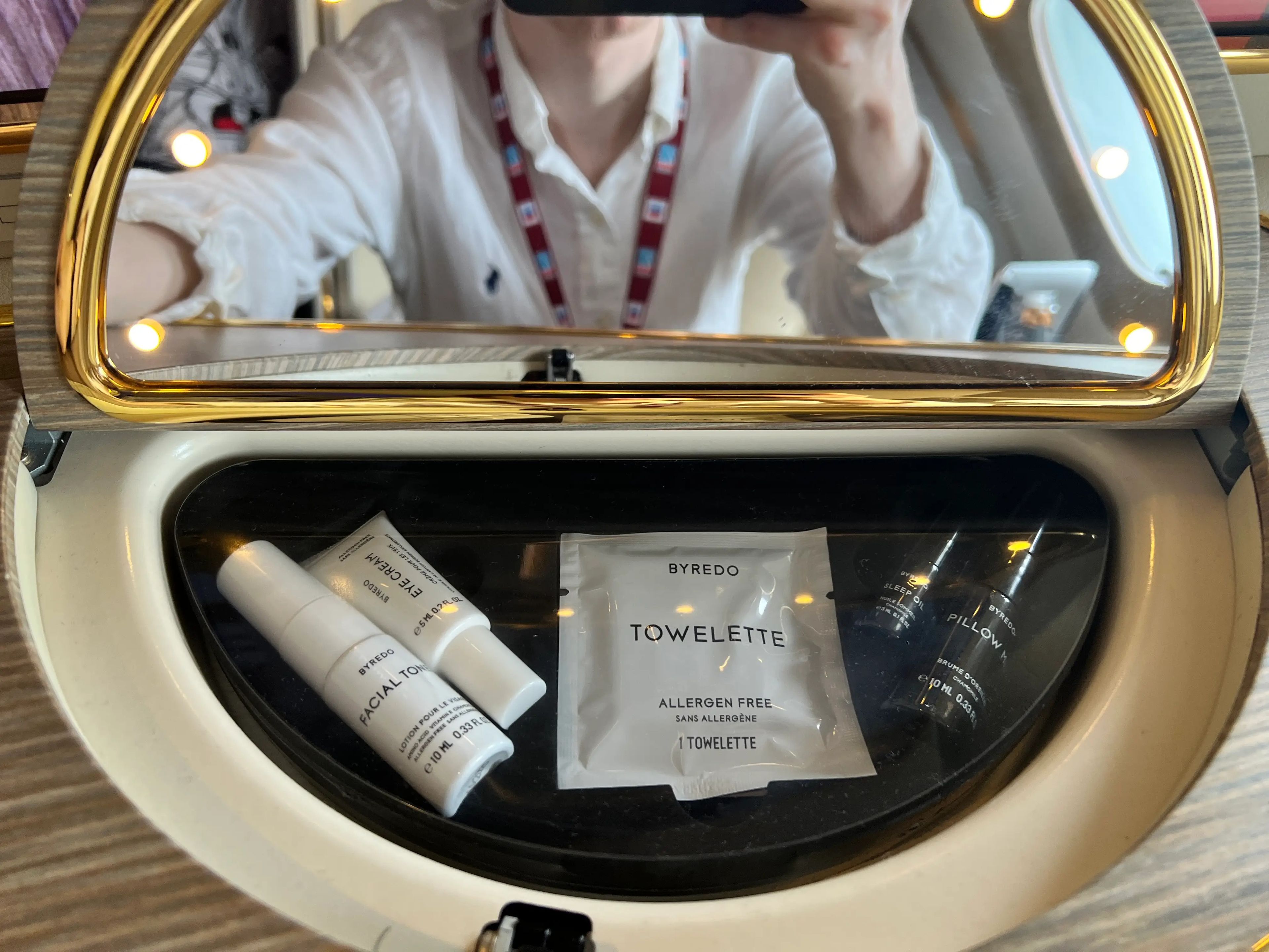A close-up of the amenities under the vanity mirror onboard Emirates A380 first class includes small black and white bottles and a packaged towelette