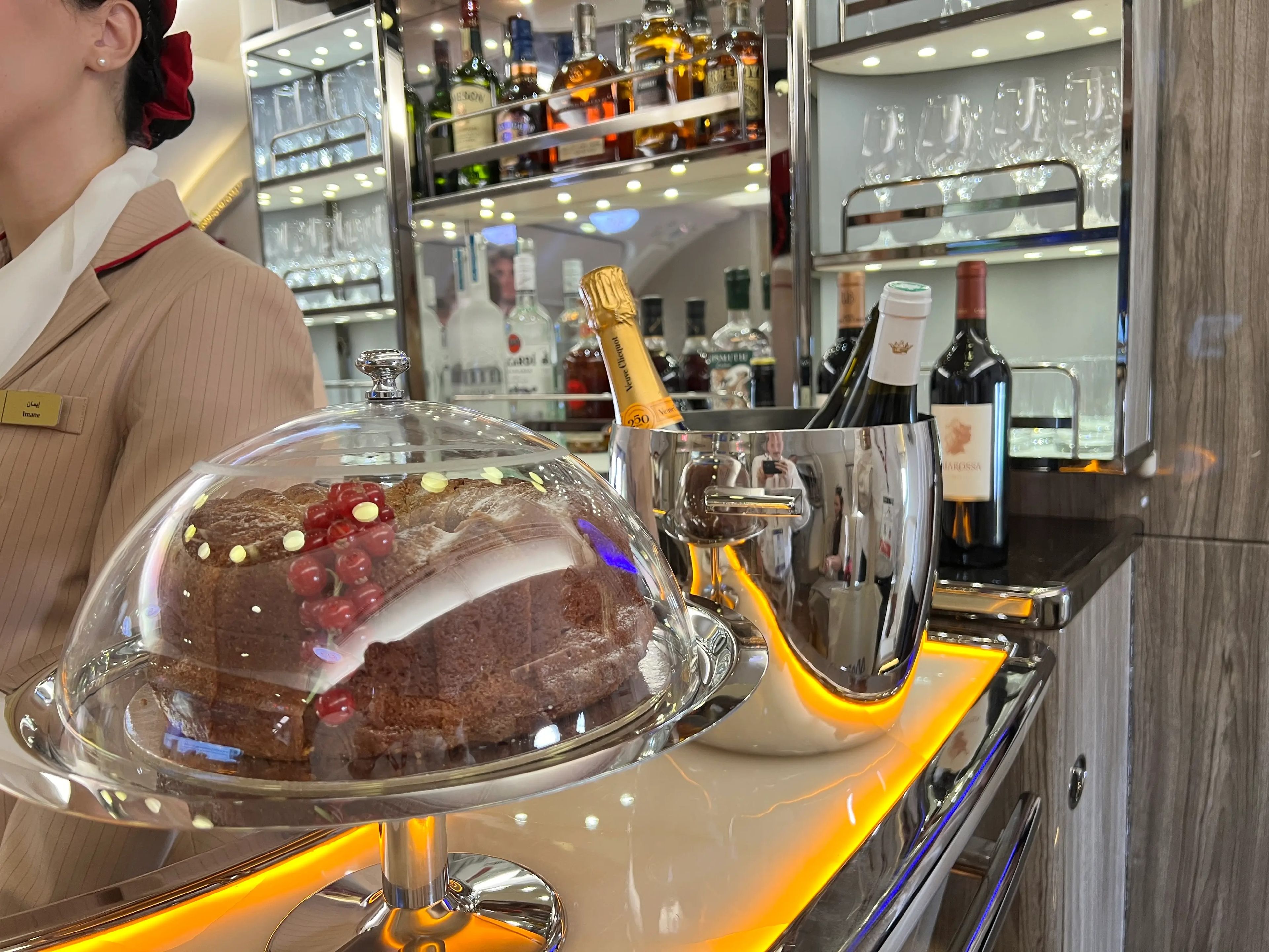 A close up of a chocolate cake on a stand and a bucket of champagne bottles on the bar on an Airbus A380.