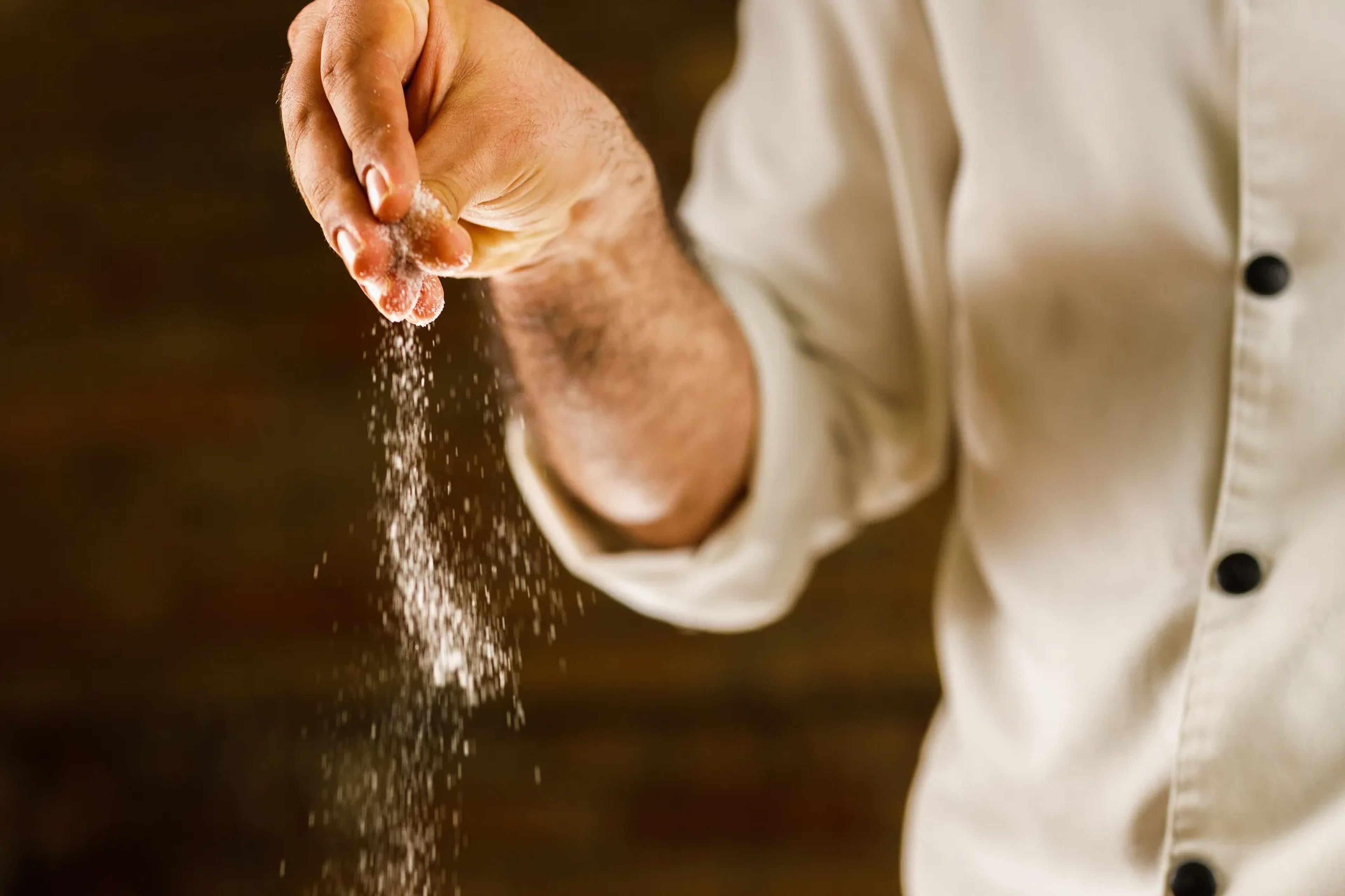 a close up of a man's hand sprinkling salt over a pot