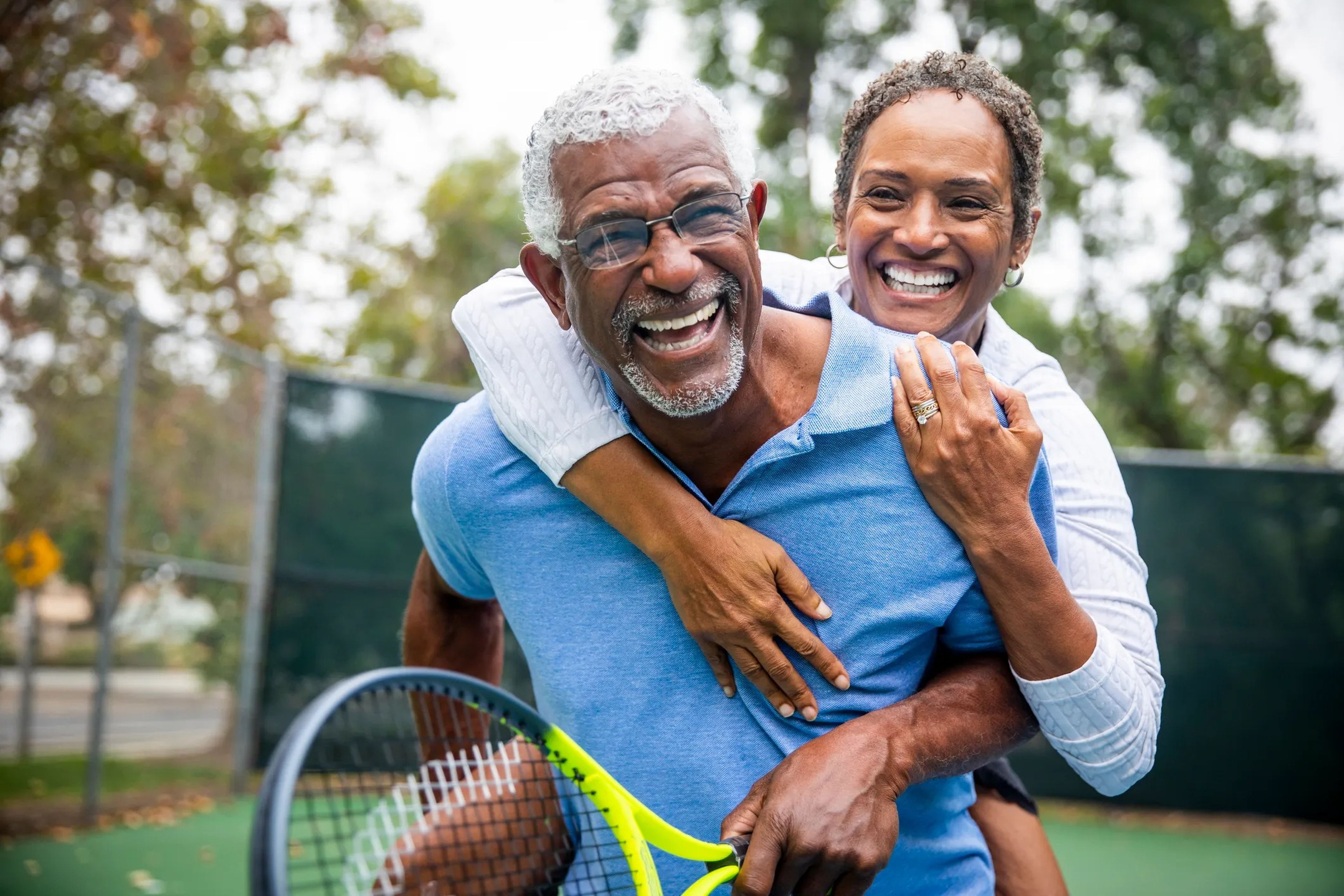 A couple with grey hair smiling on a tennis court.