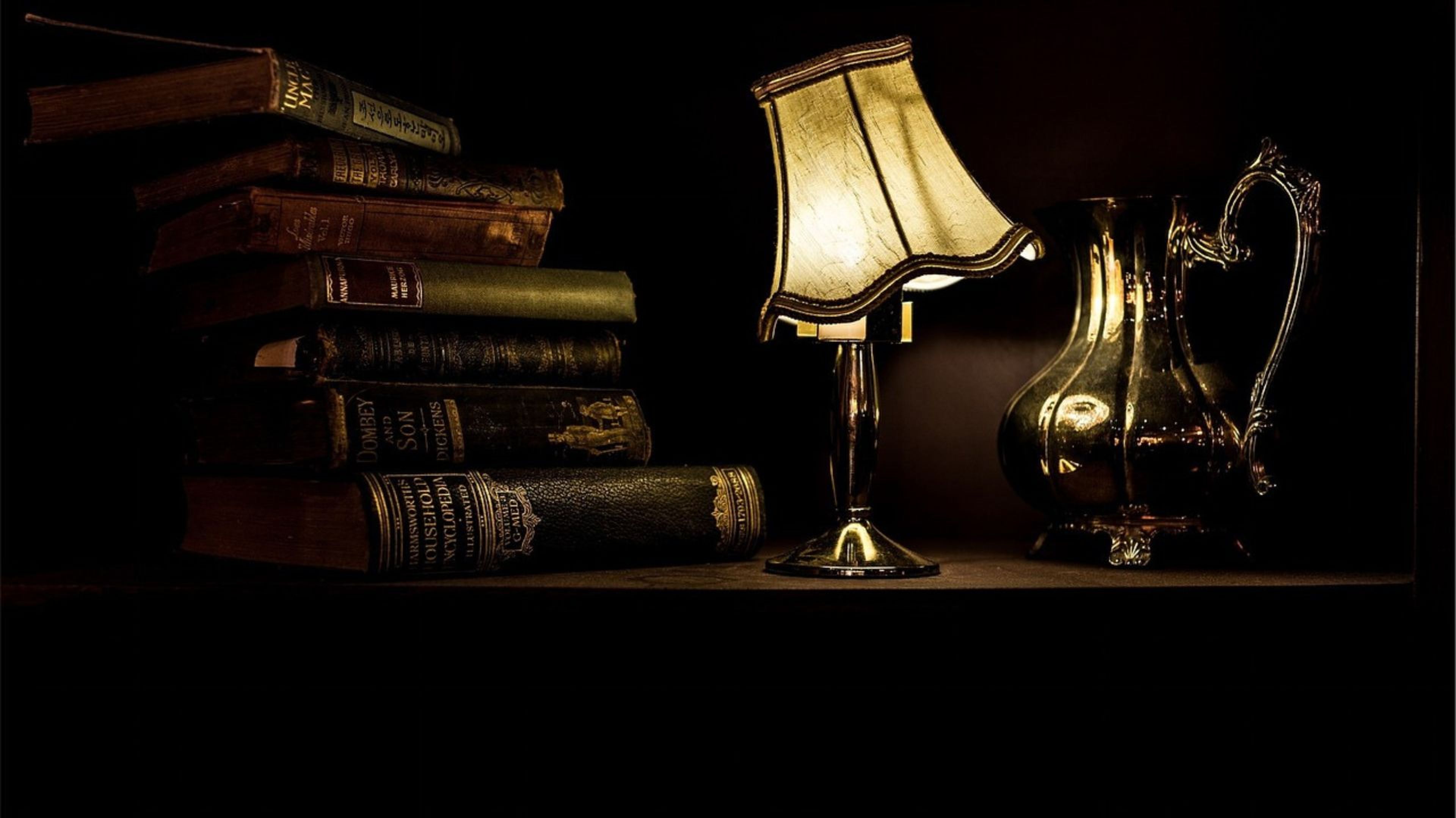 Un escritorio antiguo con una lámpara, una jarra y varios libros.