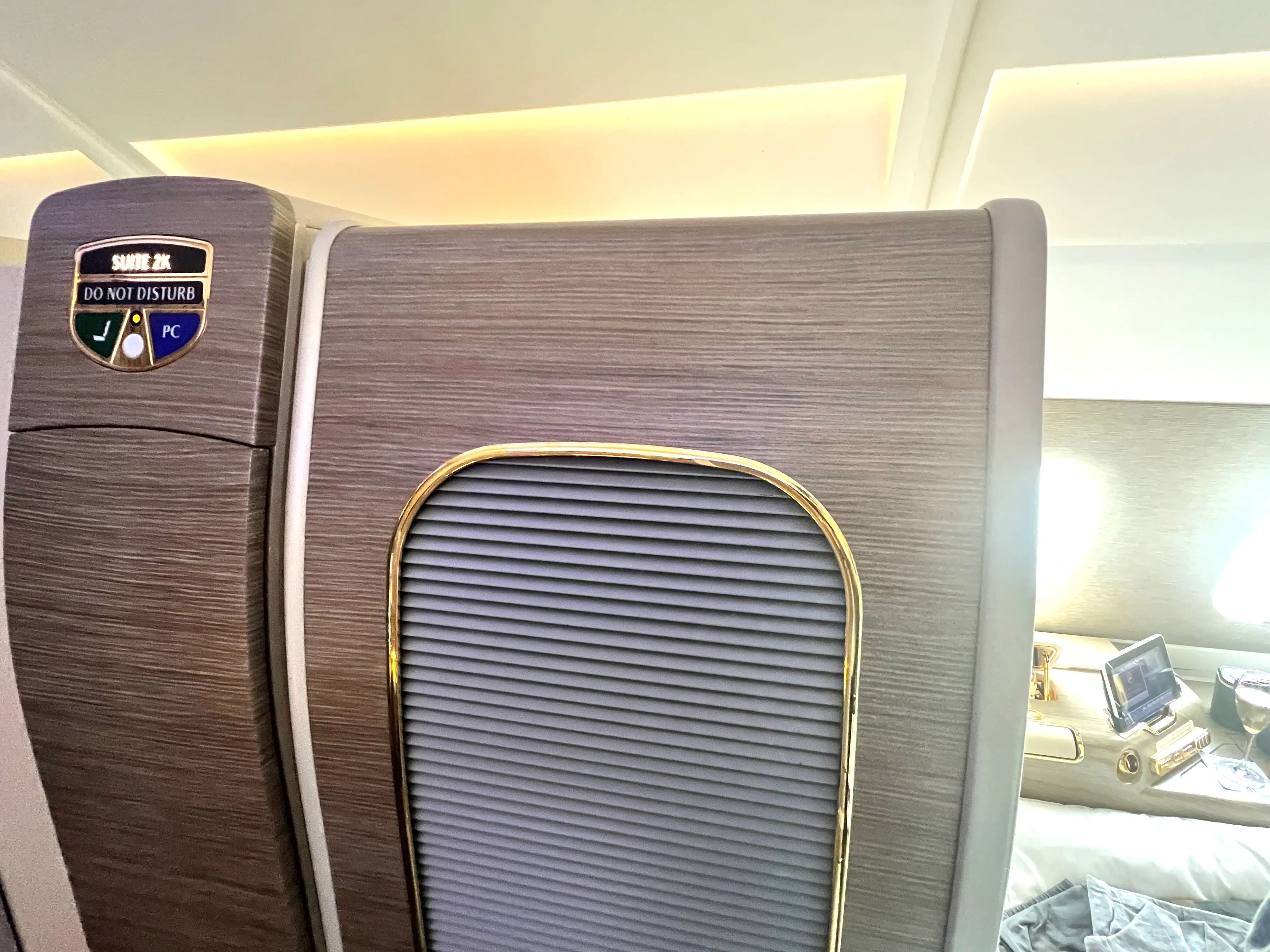 The exterior of a first-class suite on an Emirates a380 shows the light-wood door and a light-up sign