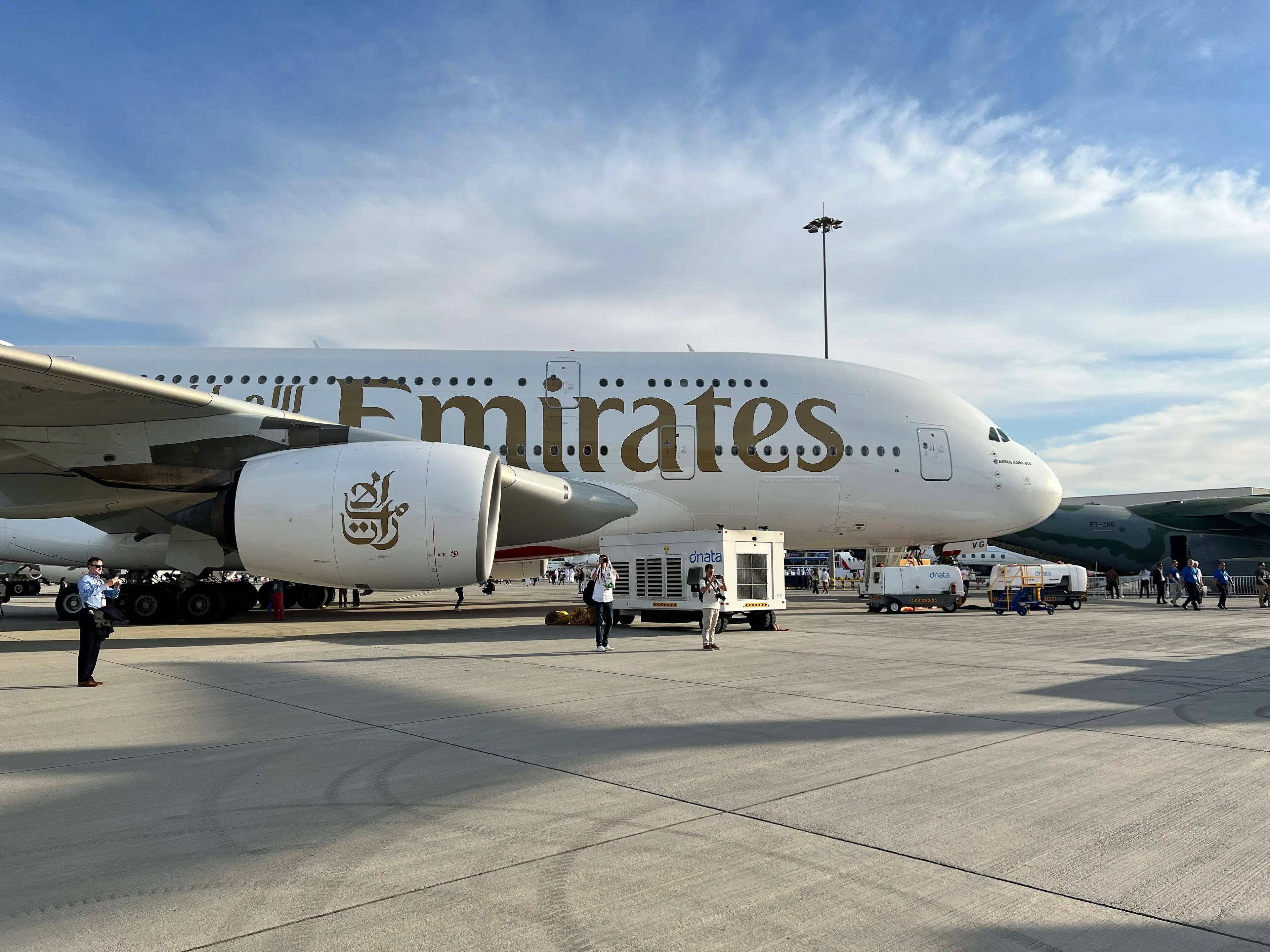 The front half of an Emirates Airbus A380 parked on the tarmac at the Dubai Airshow, with two photographers standing in front.