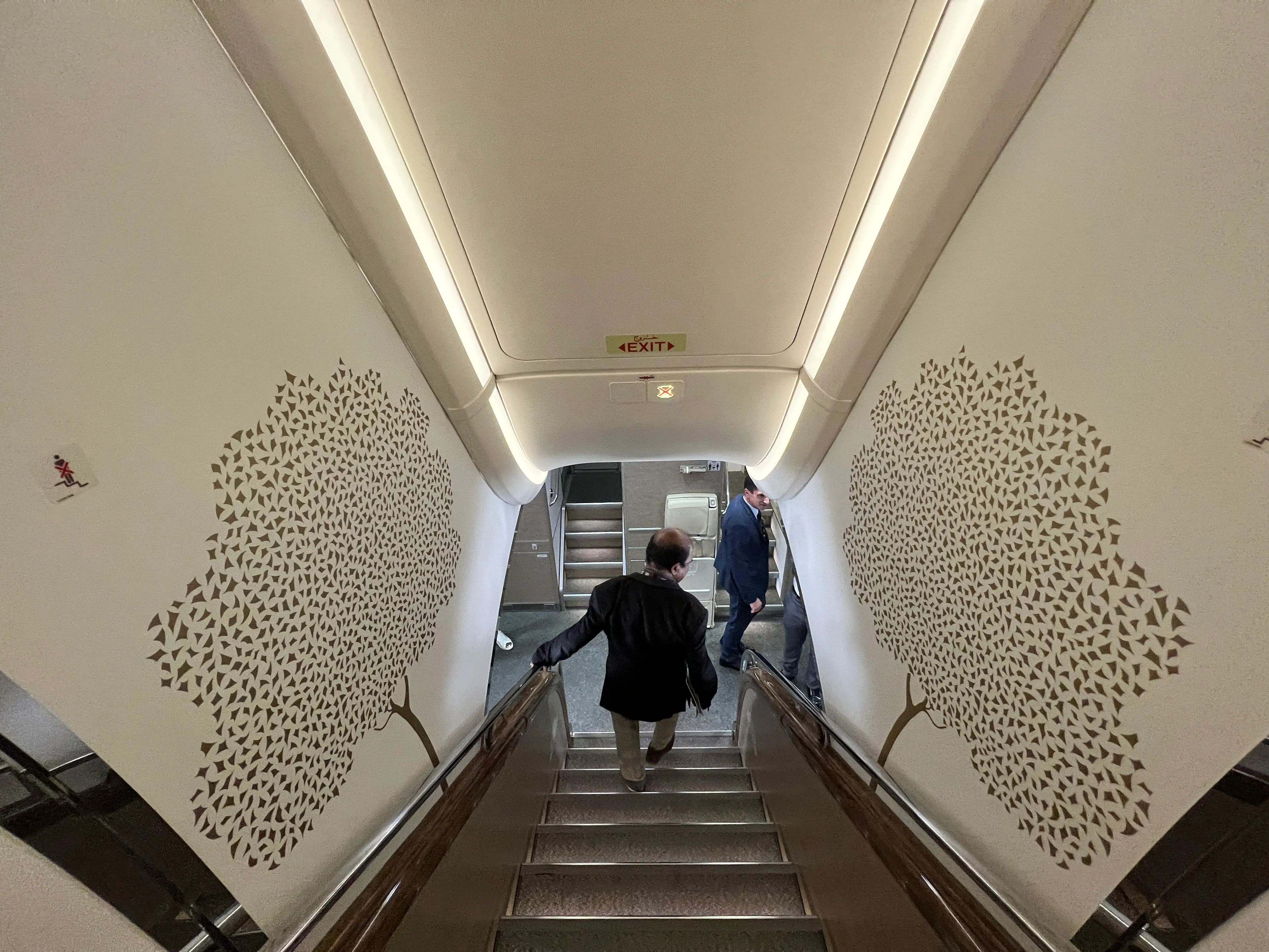 Looking down the front staircase onboard an Emirates A380, with ornate gold tree designs on the white wallpaper