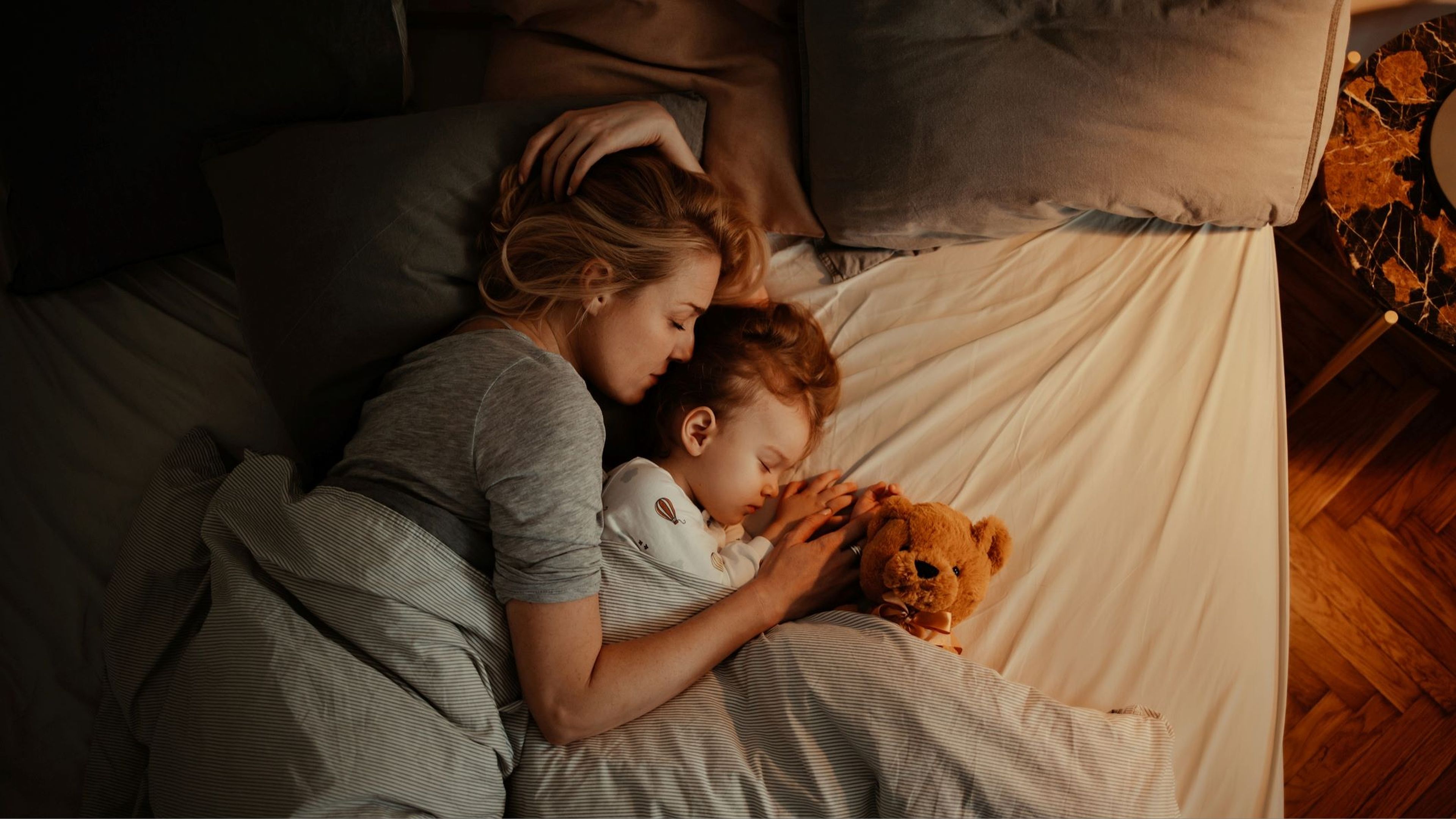 Madre e hija duermen en la cama con un oso de peluche