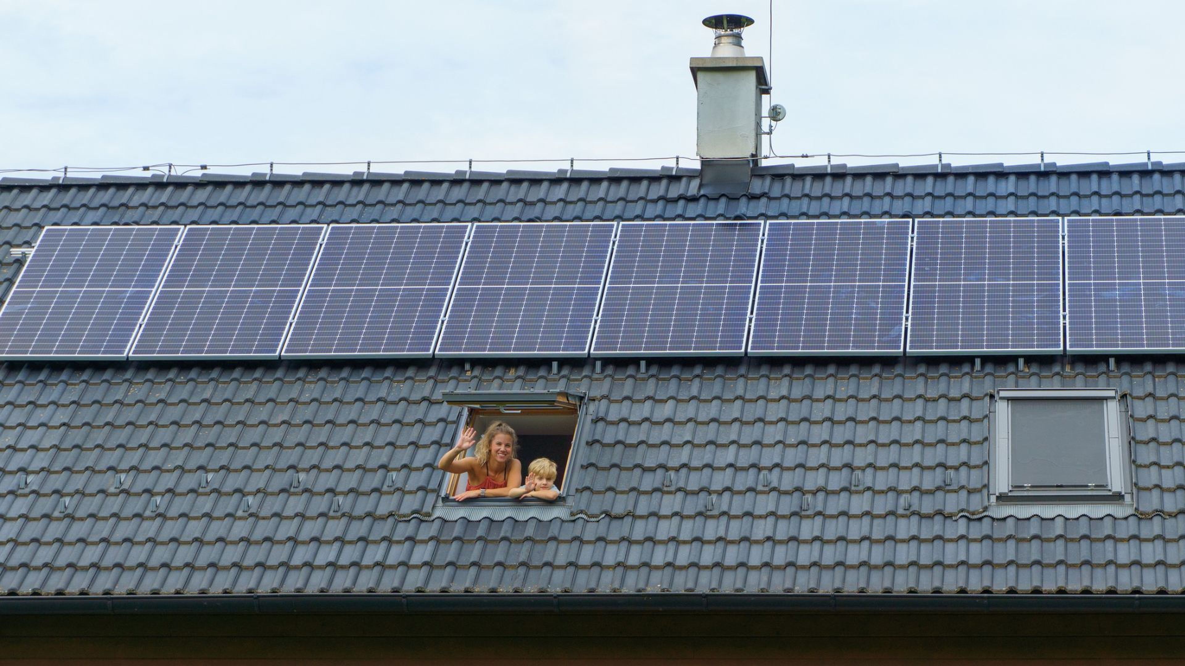 Una madre y su hijo salen por la ventana en un tejado con varias placas solares.