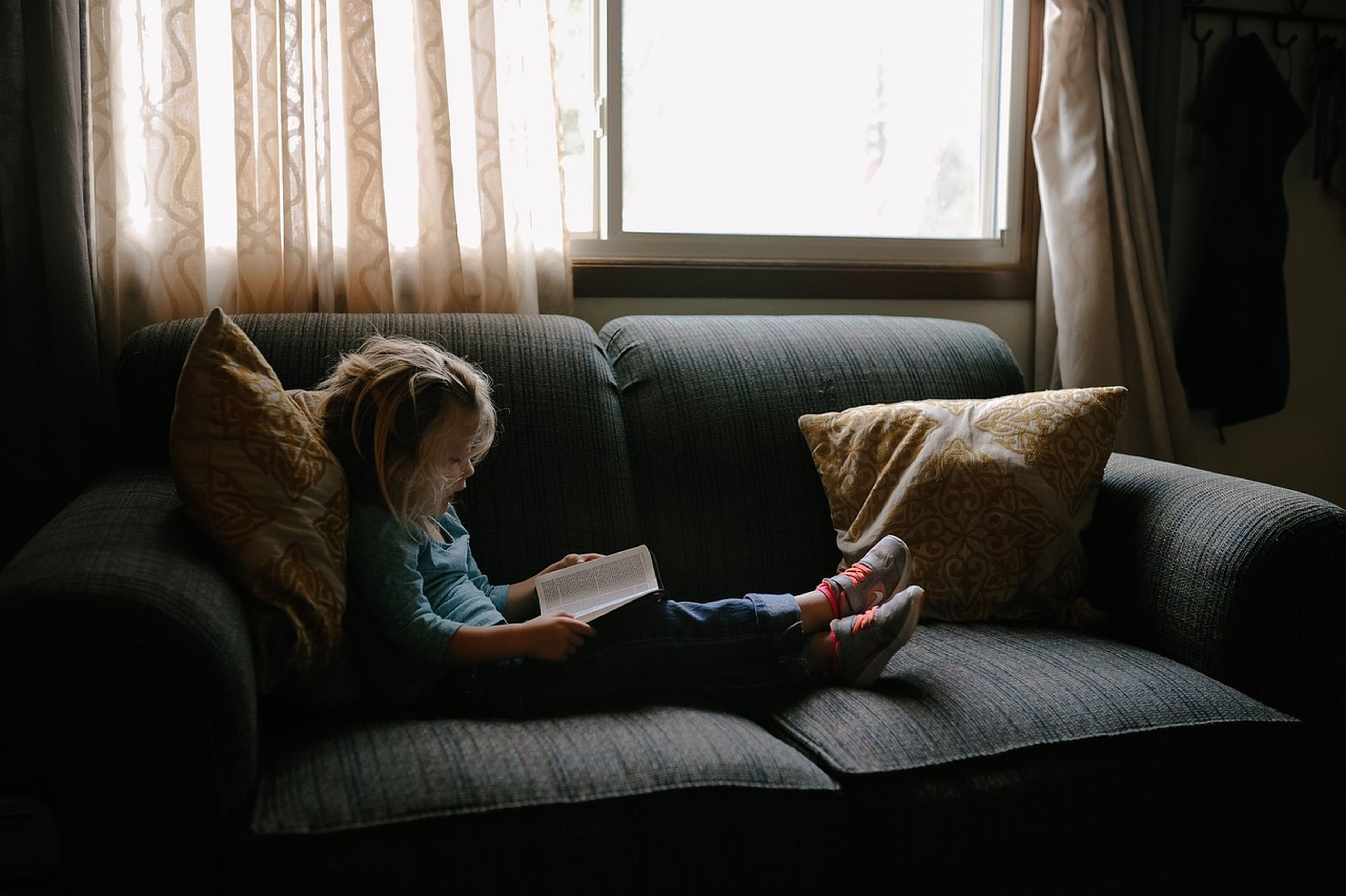 Una niña lee sentada en el sofá.