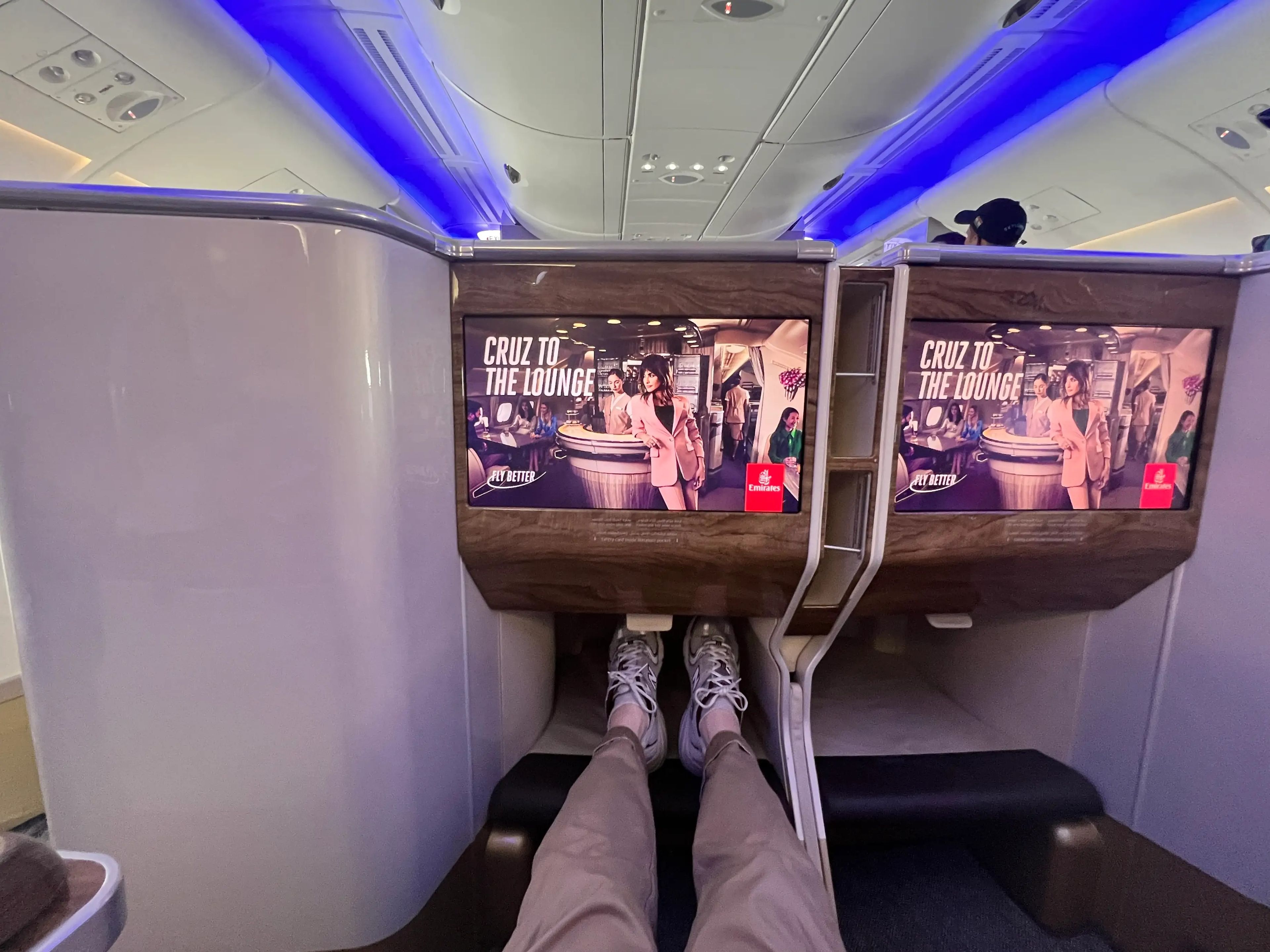 A passenger's point of view stretching out his legs and resting them on an ottoman in an Emirates business class seat, with a TV screen in front.