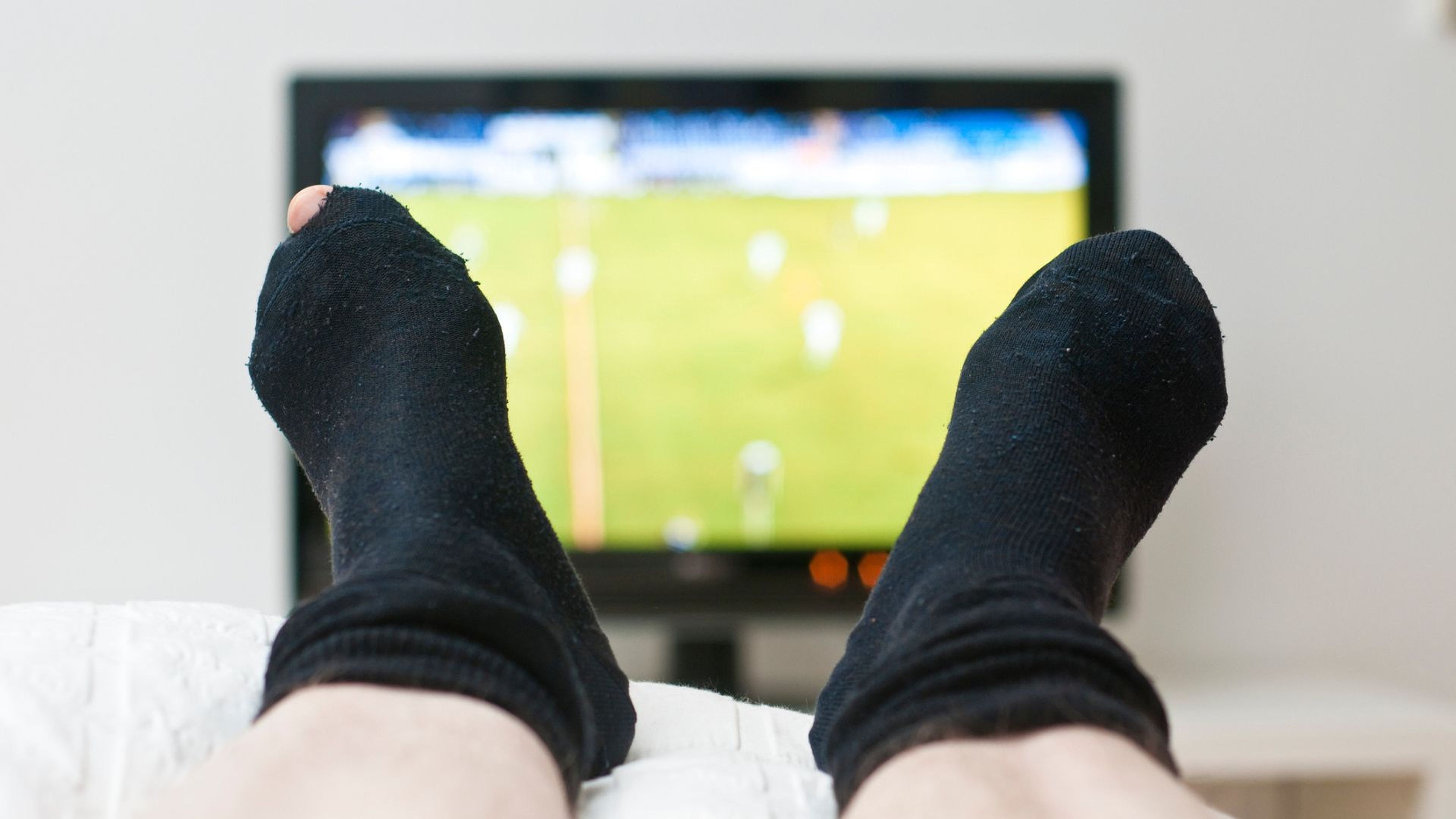 Los pies de una persona (con los calcetines rotos) que está viendo la televisión.