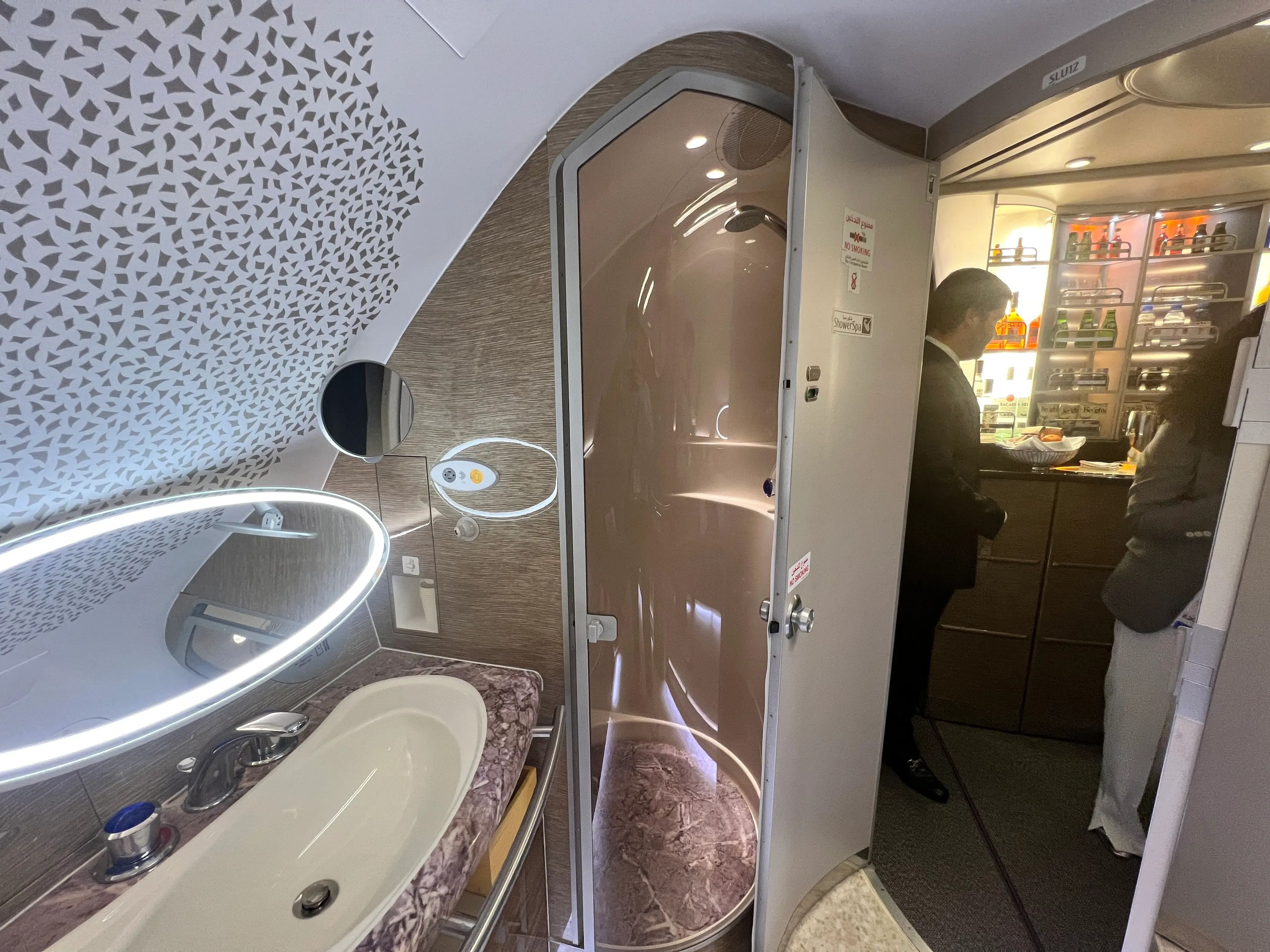 The private shower spa onboard an Emirates a380, with shower in the corner, sink to the left, and open door showing another small bar.