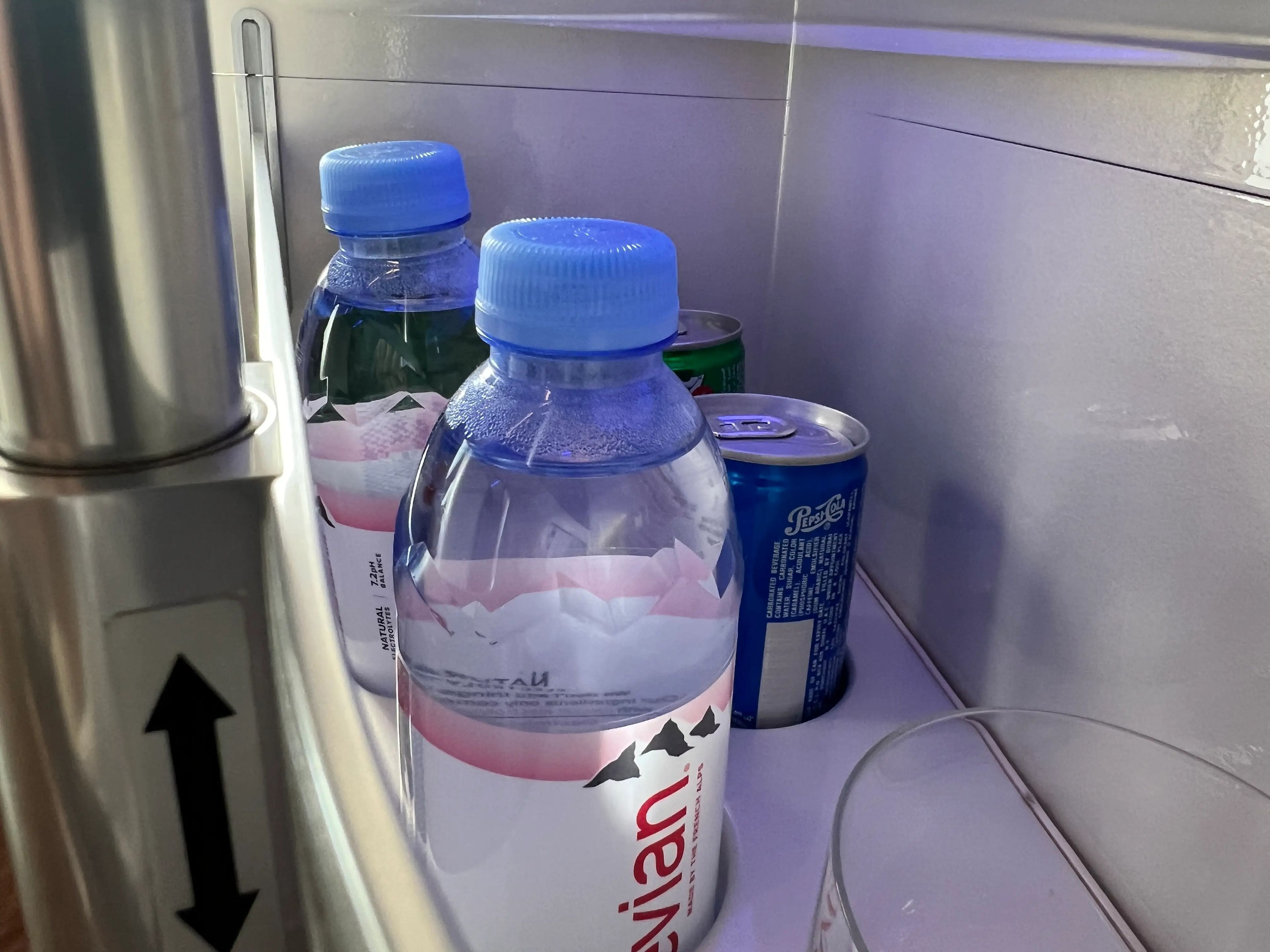 Two bottles of water, and cans of pepsi and 7up, in a holder on Emirates business class