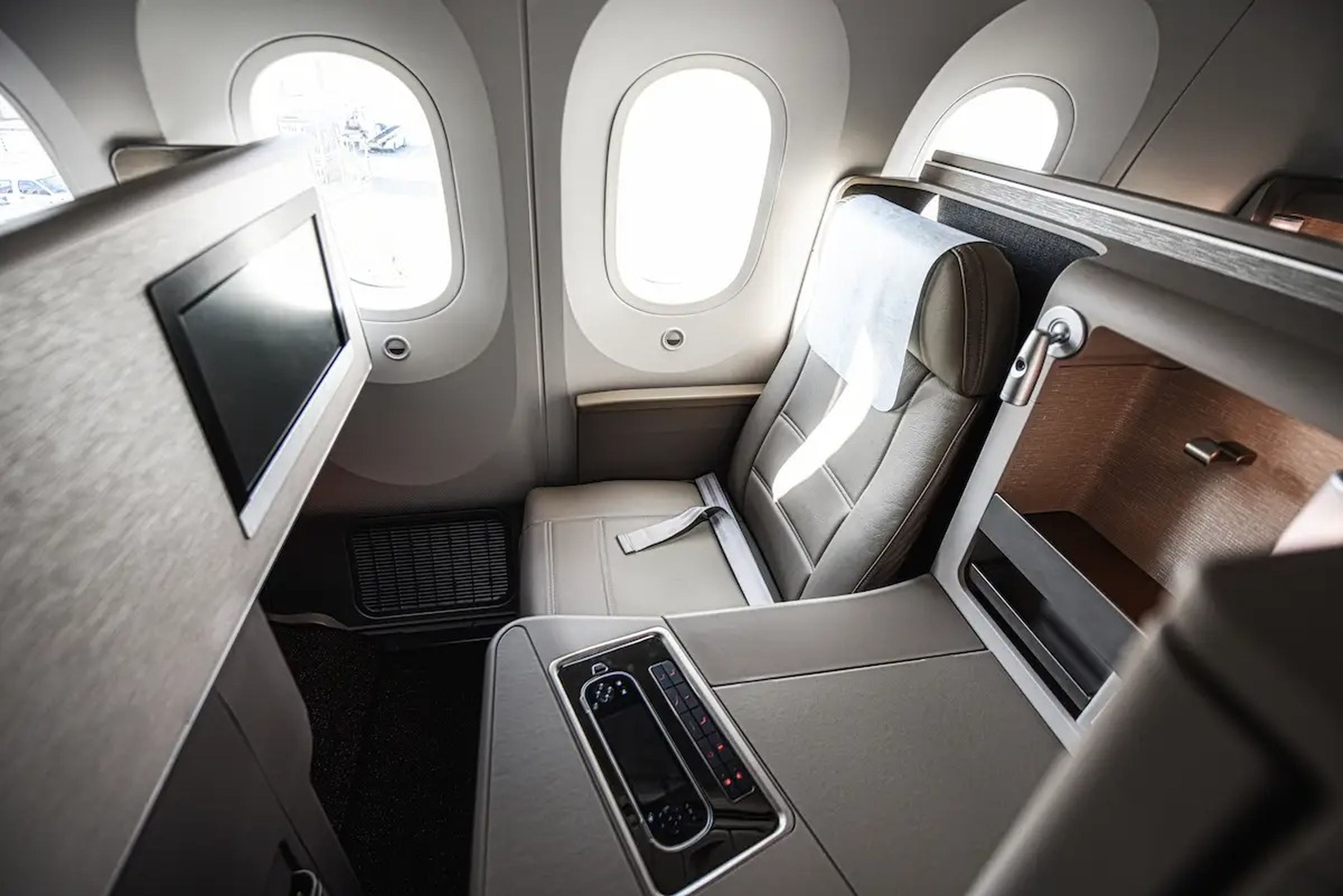 A view of a business class seat on a plane with a window, TV screen, and remote control.