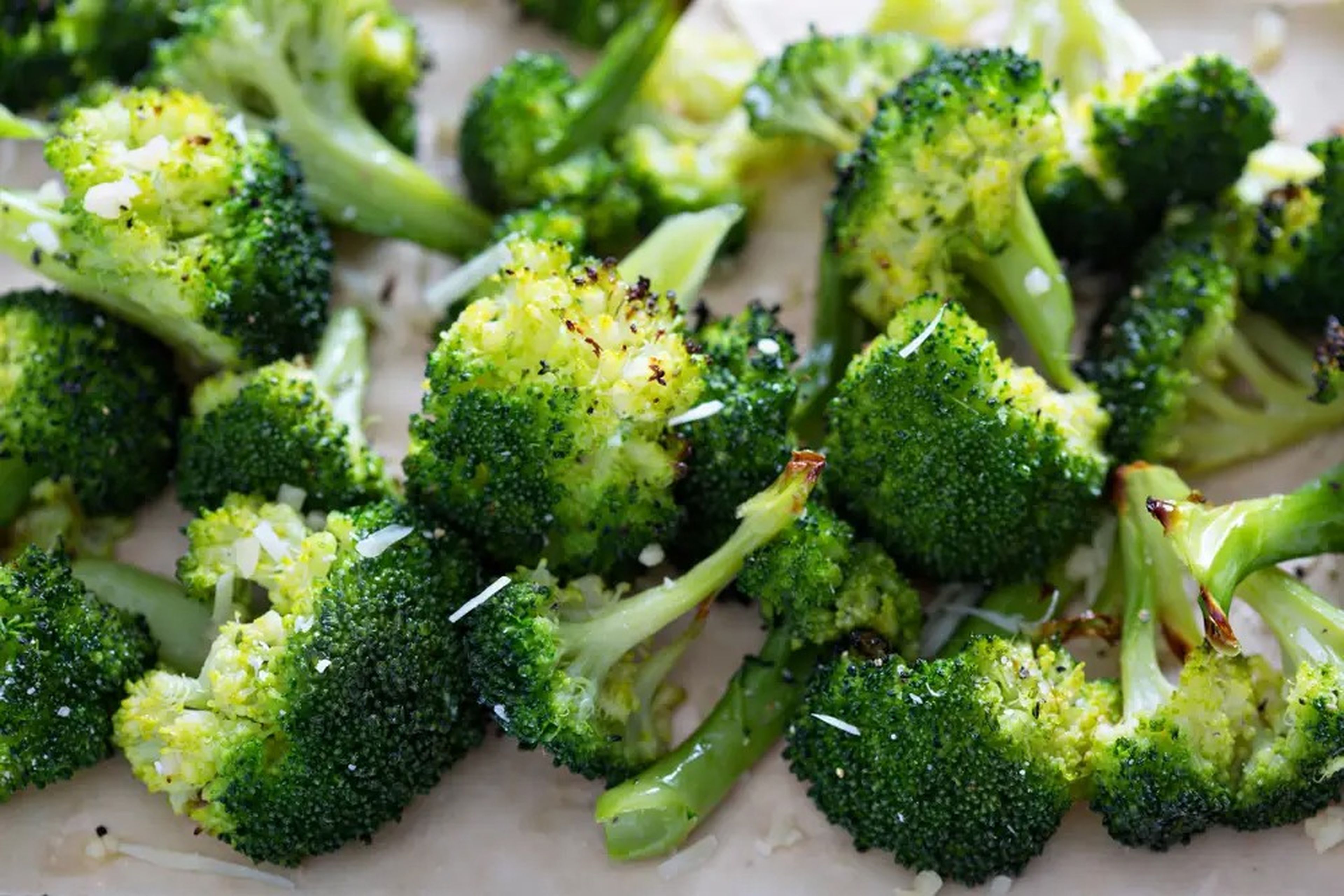 broccoli florets on parchment paper with a bit of browned parmesan sprinkled on them