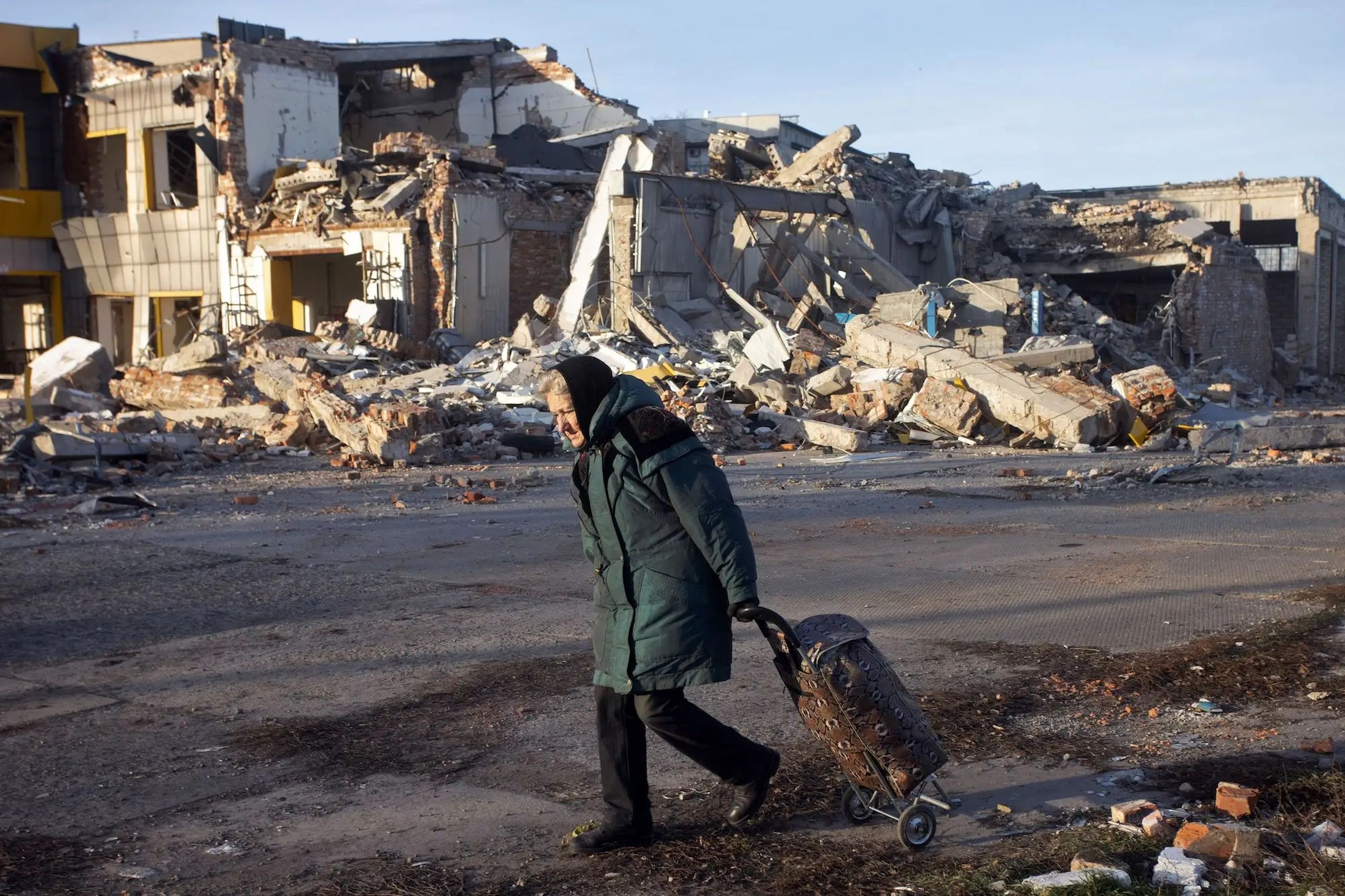Una anciana arrastra un carrito delante de un edificio destruido en Bajmut en diciembre de 2022.