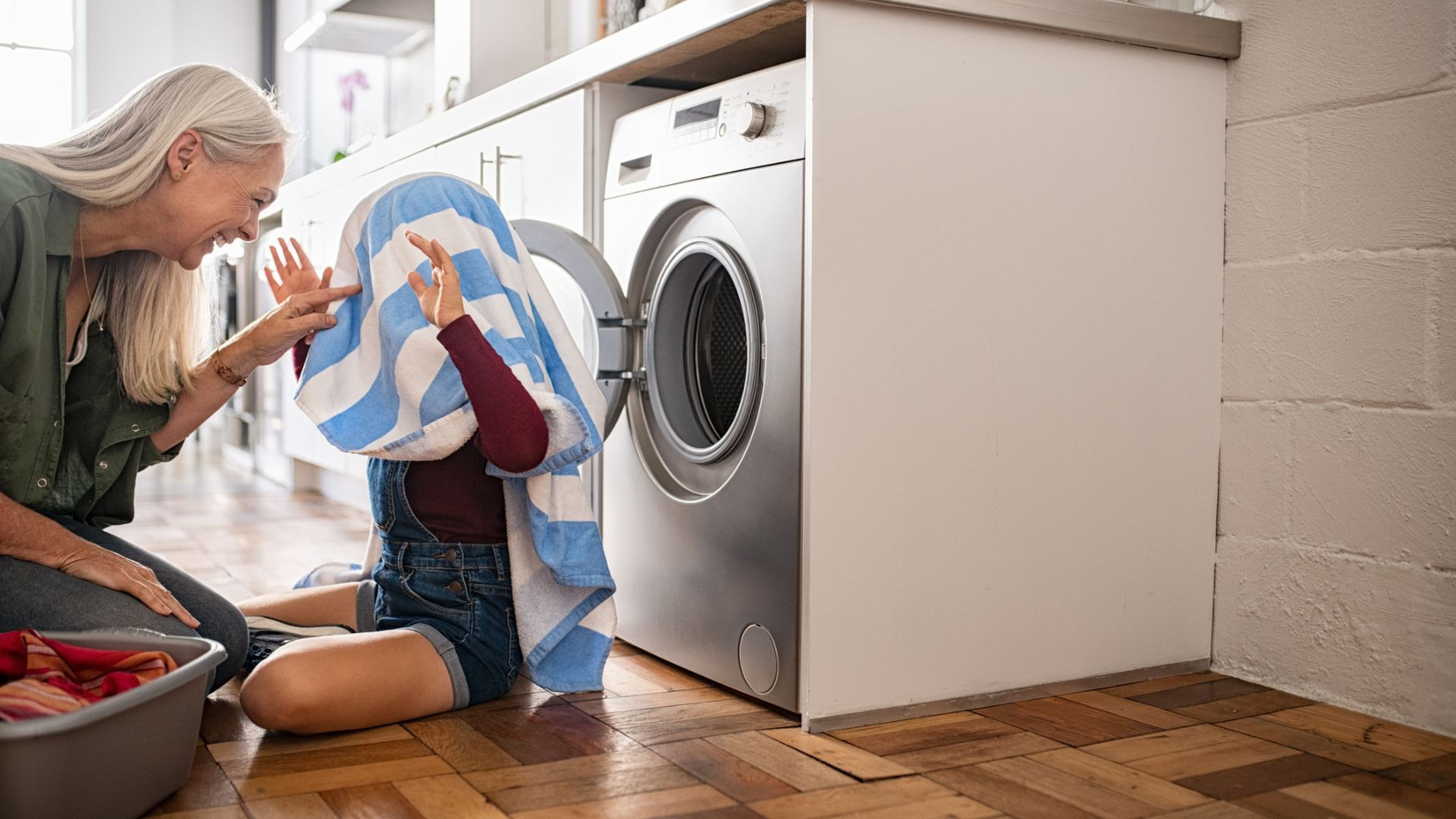 Una mujer juega con su nieta delante de la lavadora.
