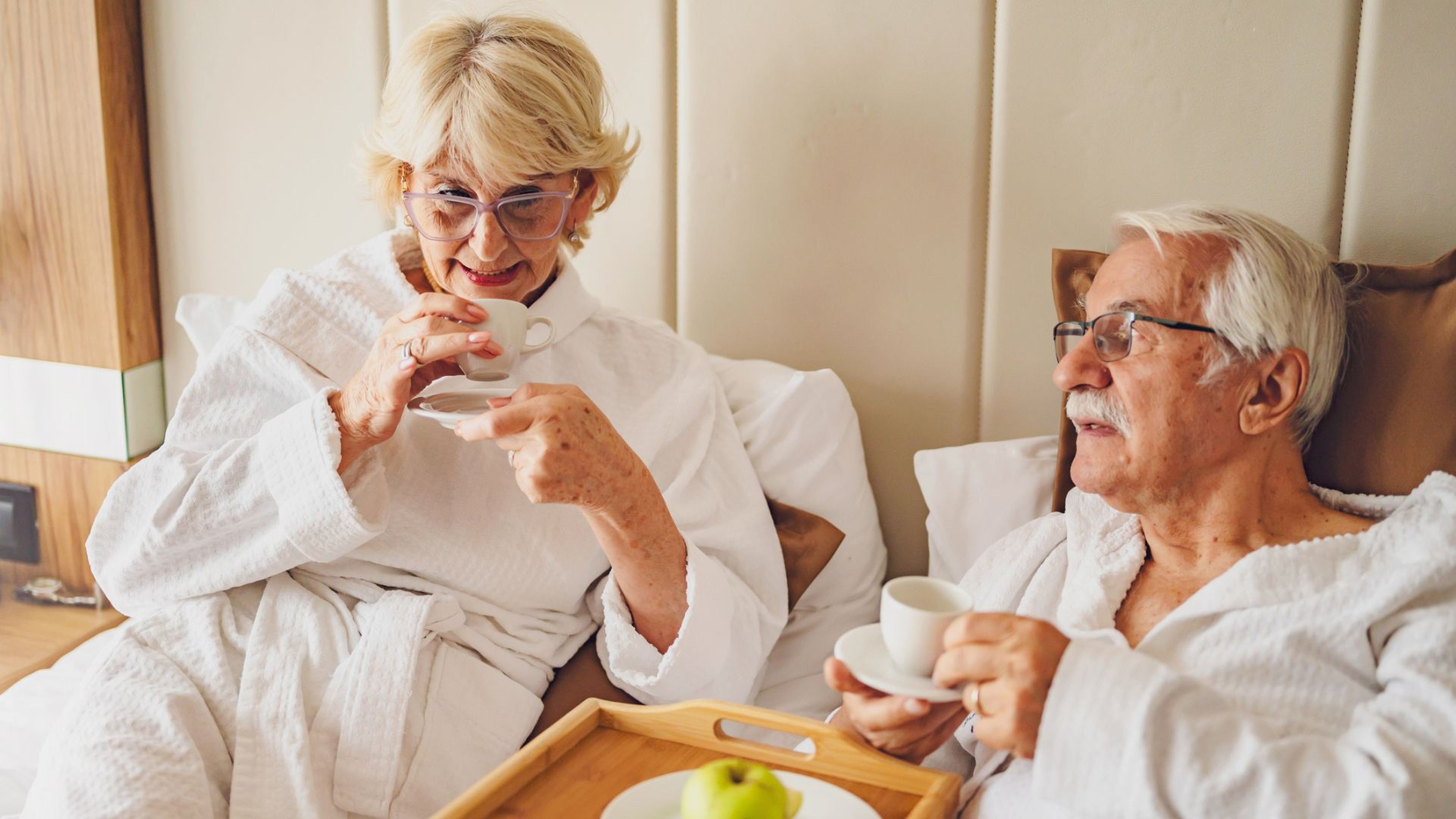 Una pareja de avanzada edad desayuna en la cama.