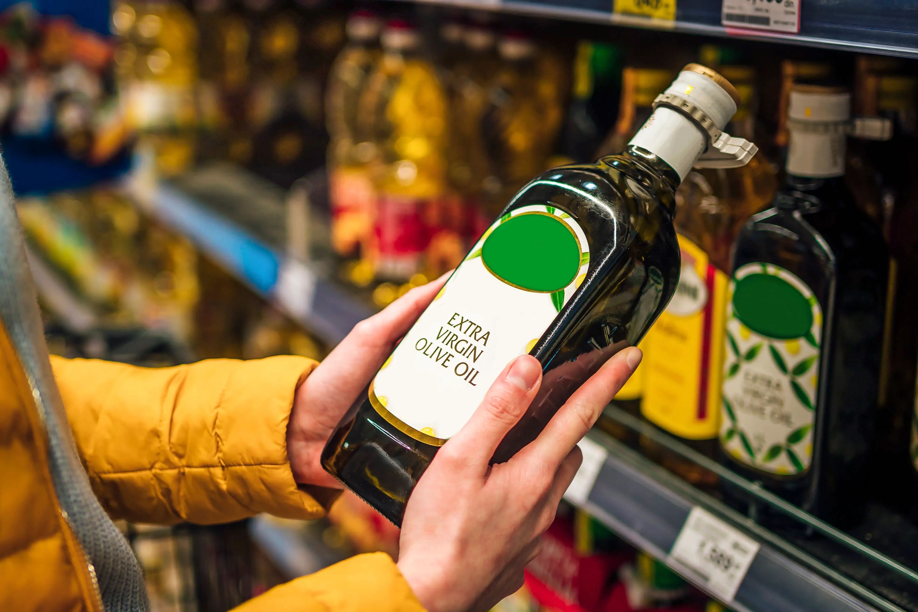 A woman chooses a bottle of extra virgin olive oil from a supermarket shelf