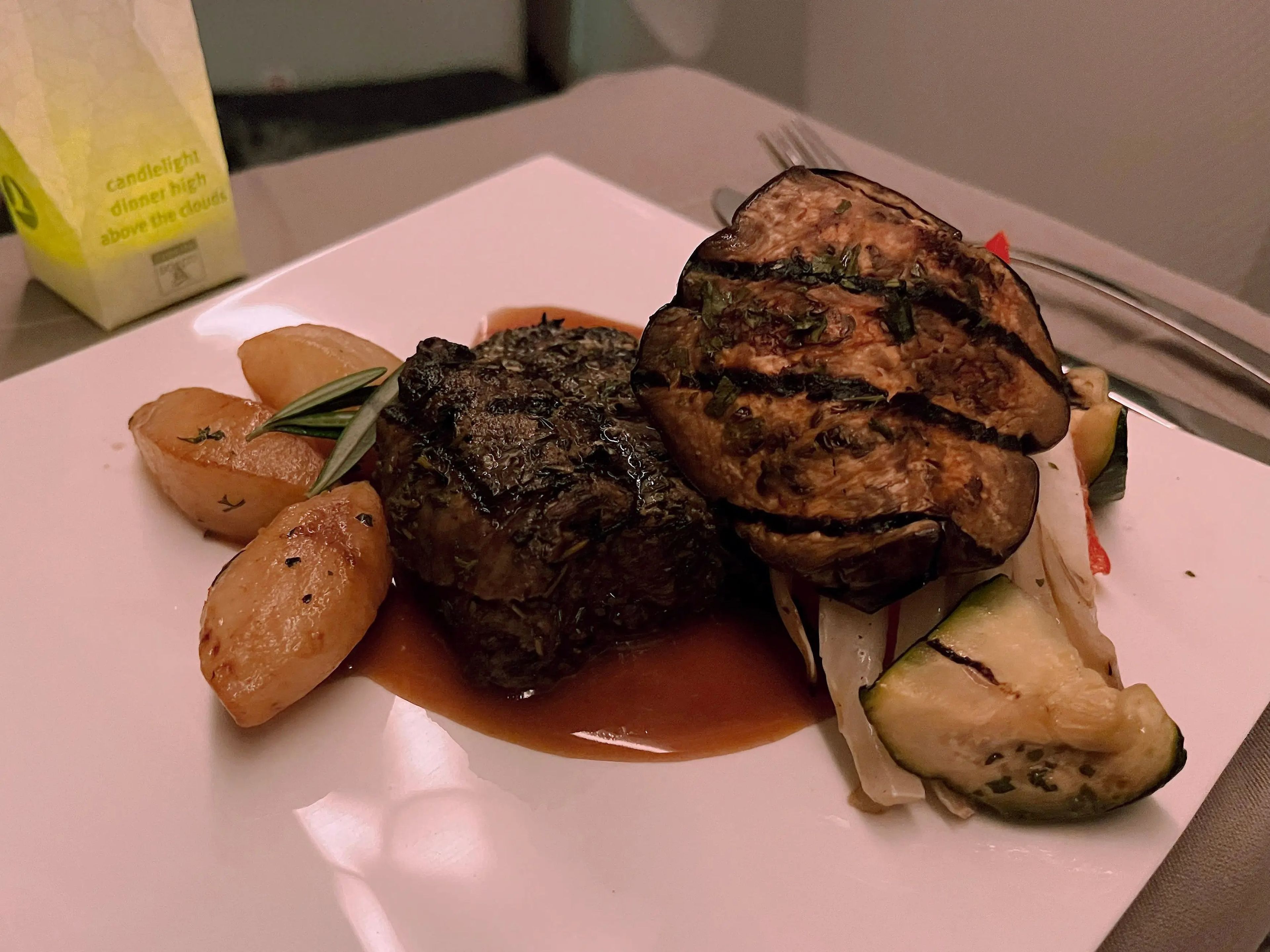 Beef filet with potatoes, onions, and zucchini on a square plate on a tray