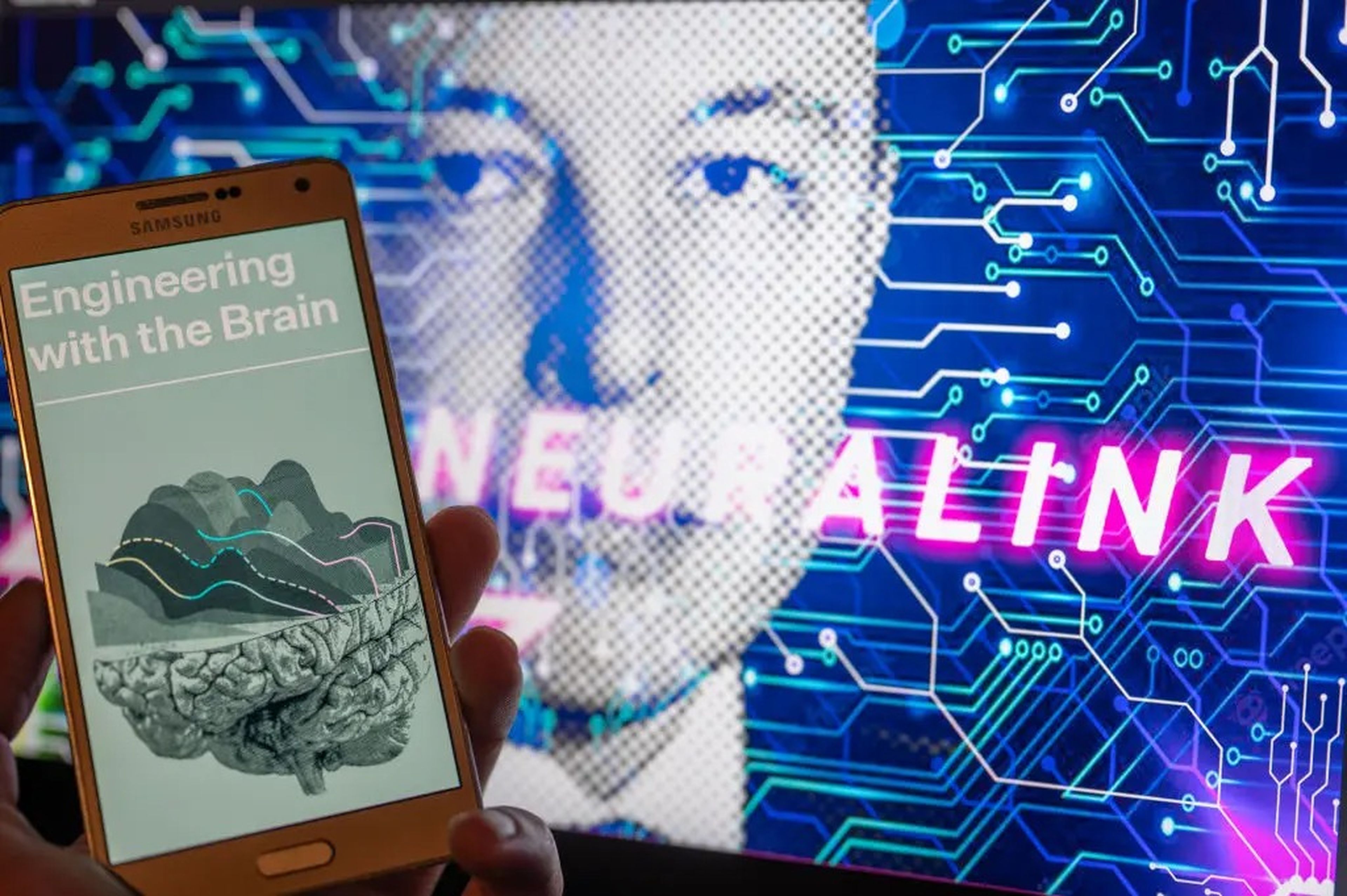 A hand holding a phone displaying a graphic that says, "Engineering with the Brain," in front of an image of Elon Musk with text saying, "Neuralink."