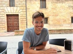 Jeronimo Noriega sitting outside at a café table in Spain while smiling.