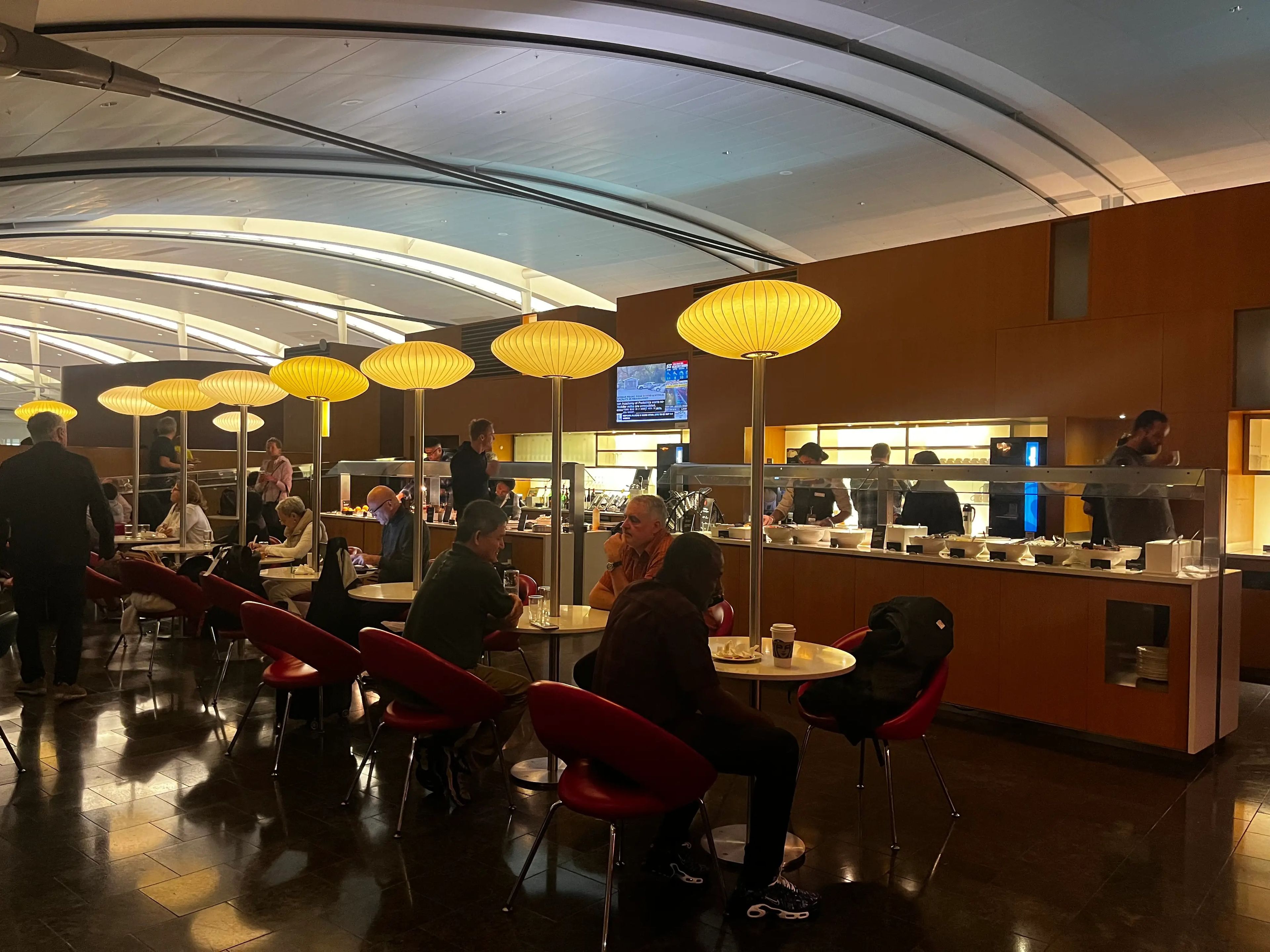 Lounge in airport filled with round tables with oblong light fixtures above them