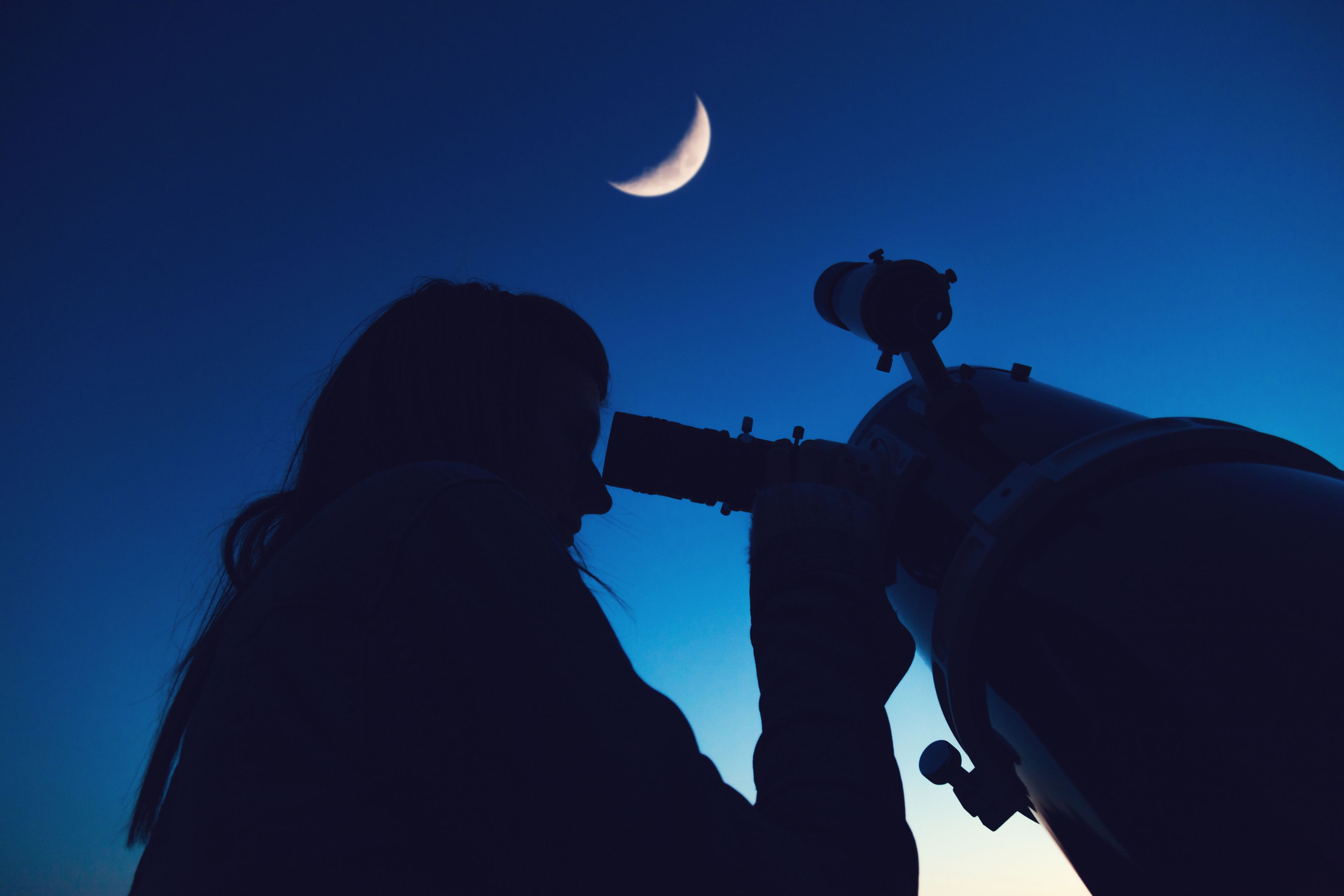 Mujer mirando la Luna a través de un telescopio