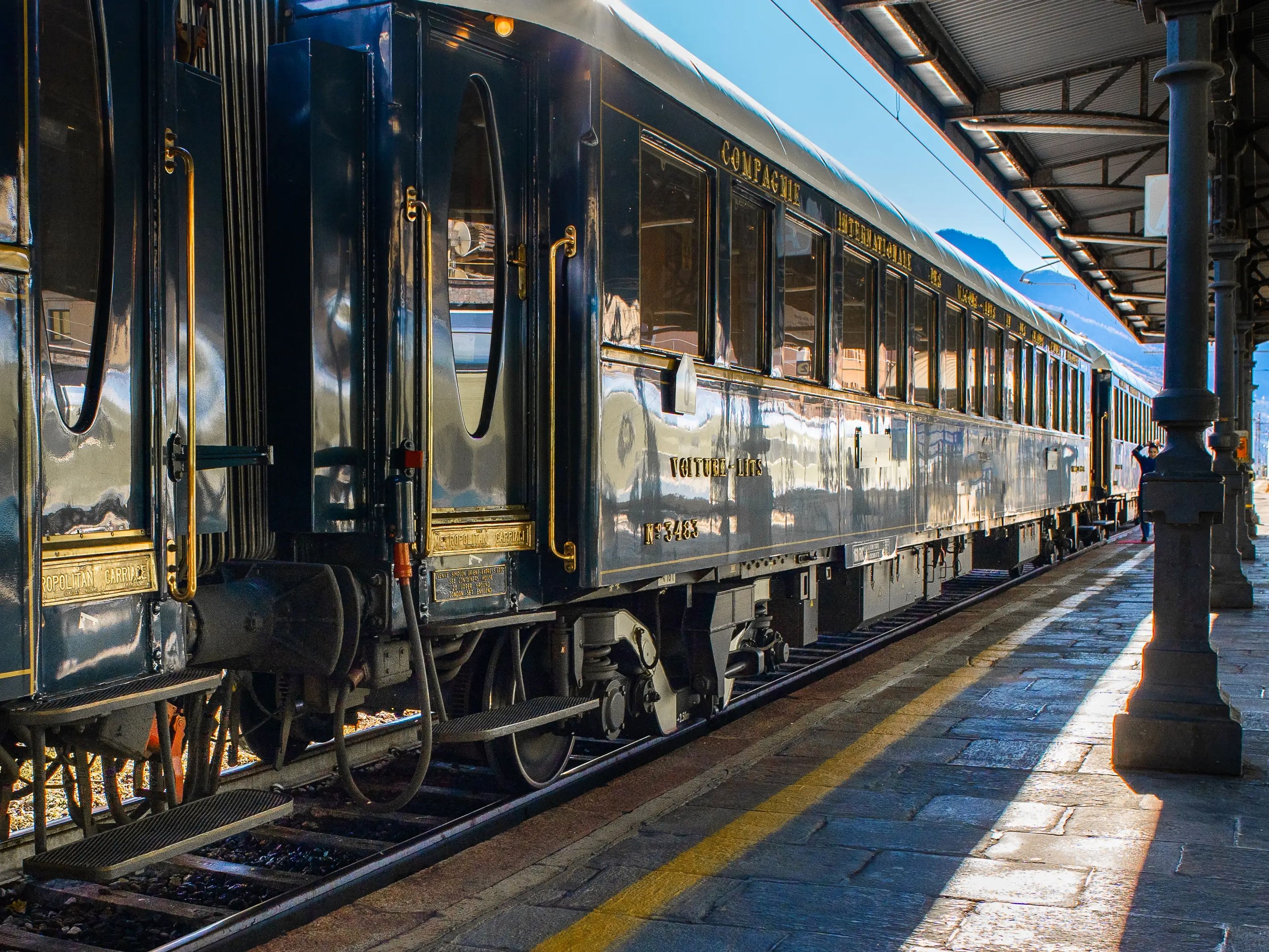 A navy blue train parked at a platform with mountains in the background
