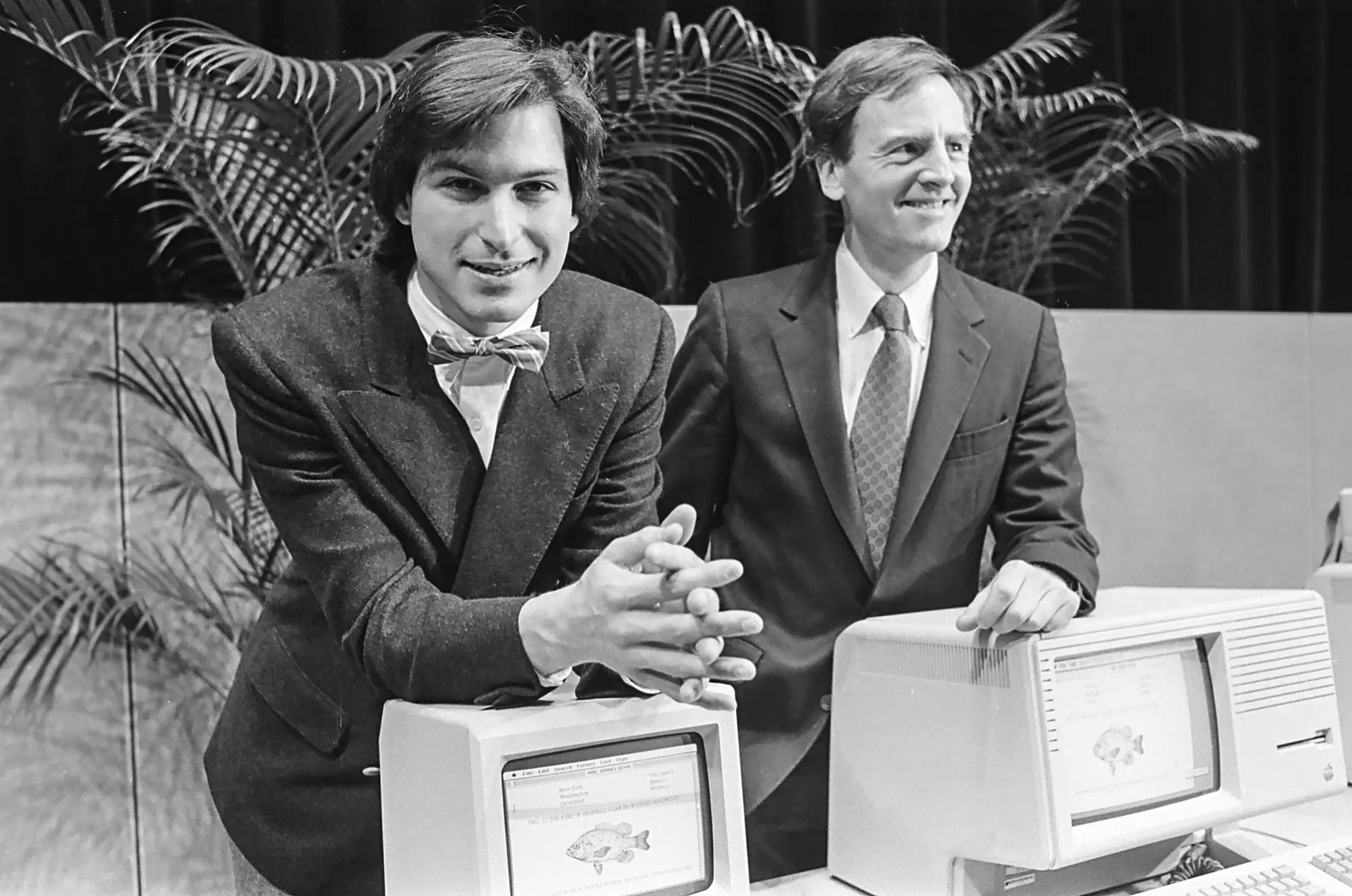 Steve Jobs, a la izquierda, y John Sculley. Sculley se apoya en el ordenador personal Apple "Lisa", sucesor del Macintosh original, sobre el que se apoya Jobs.